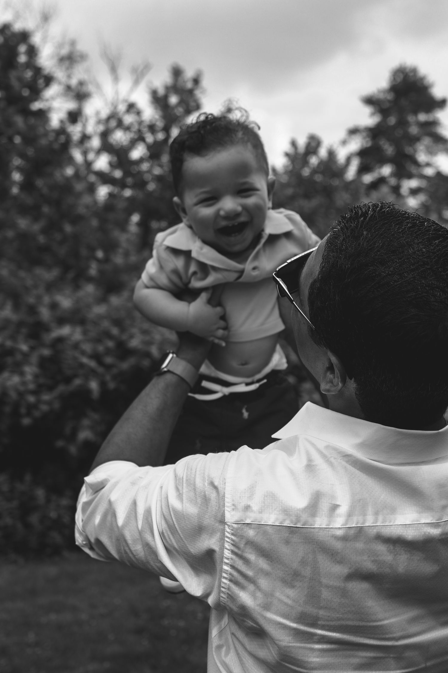 A series of black and white photos showing a parent lifting and playing with a joyful baby outdoors.