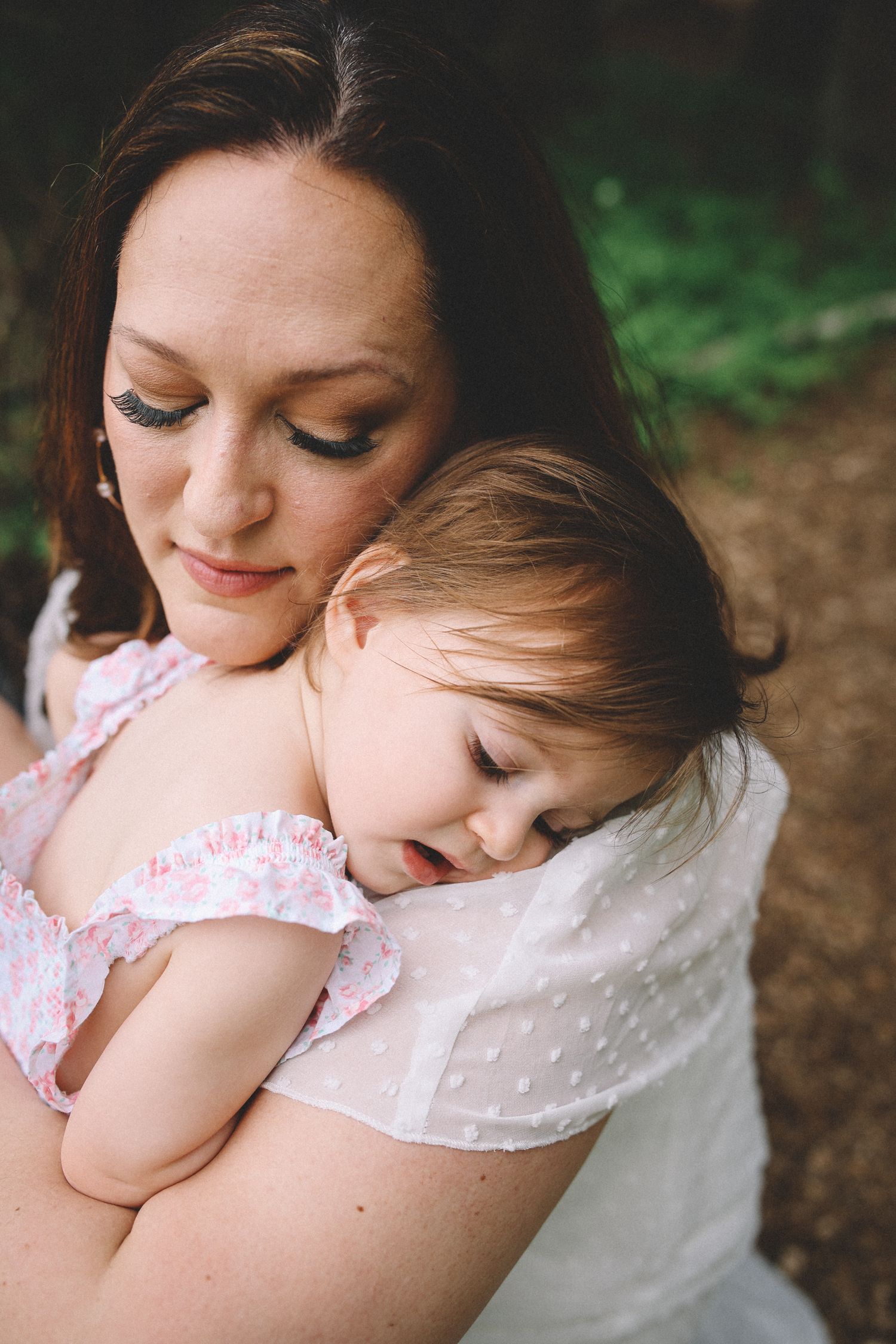 A tender moment shows a parent in white embracing a small child in pink against a blurred natural background.