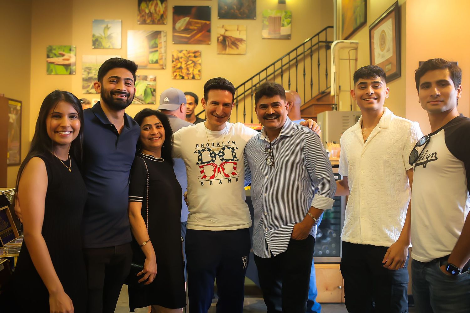 A group of people standing together in a casual indoor setting with framed pictures on the wall behind them.