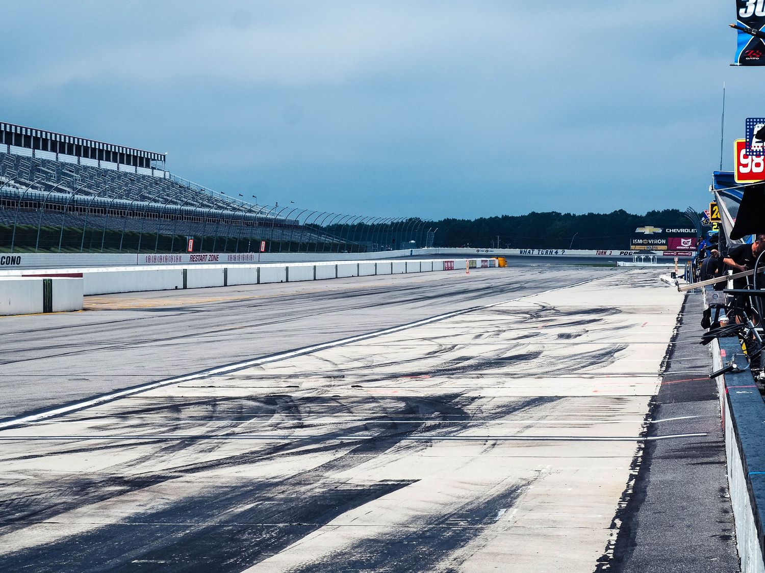 Panoramic view of an empty race track with grandstands and cloudy skies at a motorsports facility.