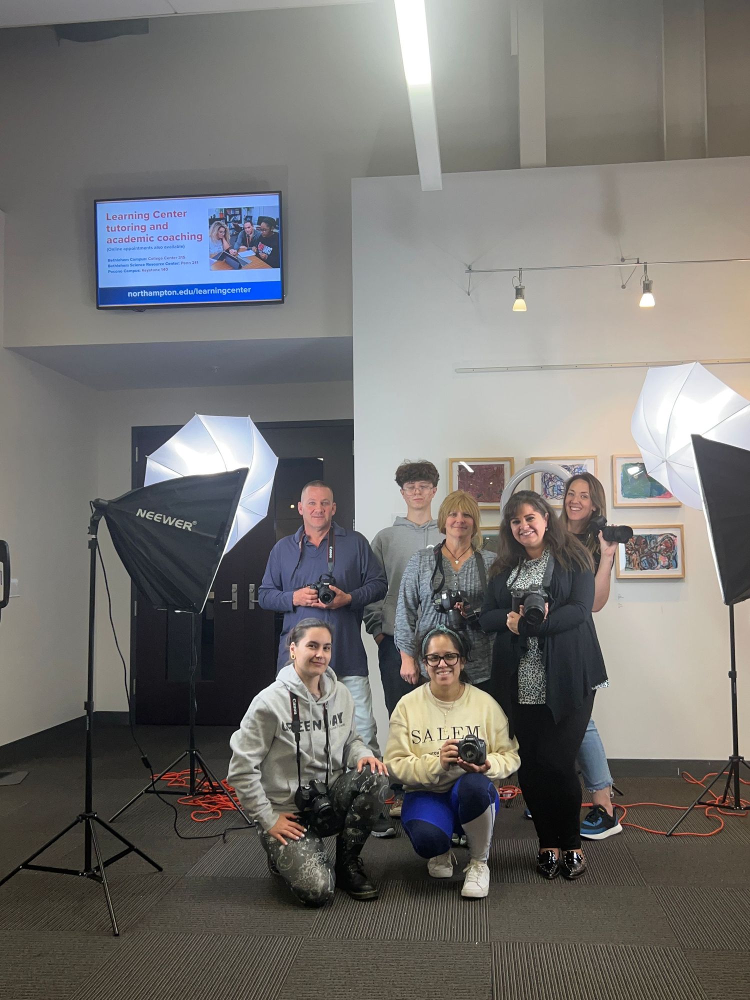 A photography studio setup with lighting equipment, backdrop stands, and people gathered in a professional workspace.