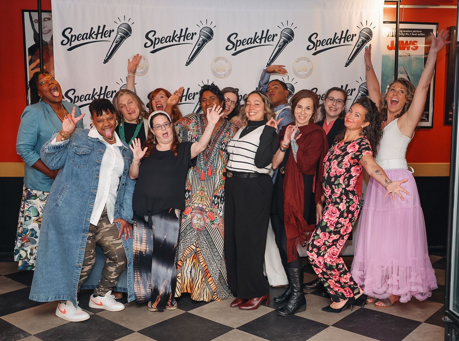 Group of women celebrating at a SpeakHer event, posing energetically in front of a branded backdrop.