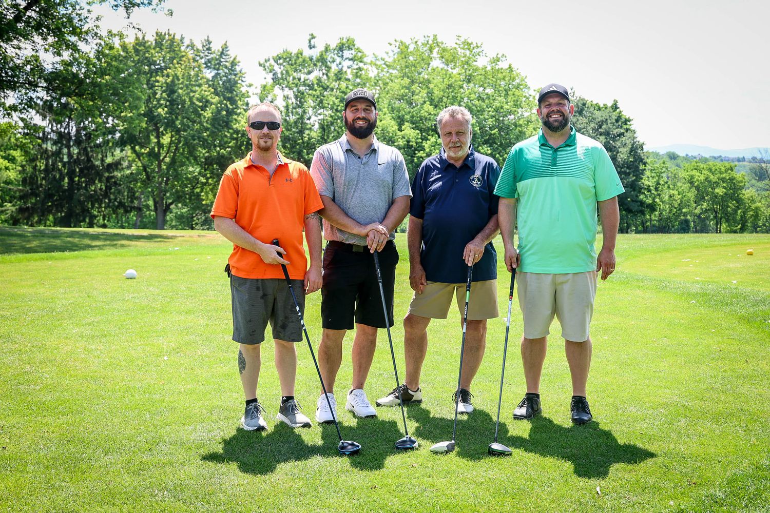 Four men posing with golf clubs on a sunny green golf course on a bright summer day.