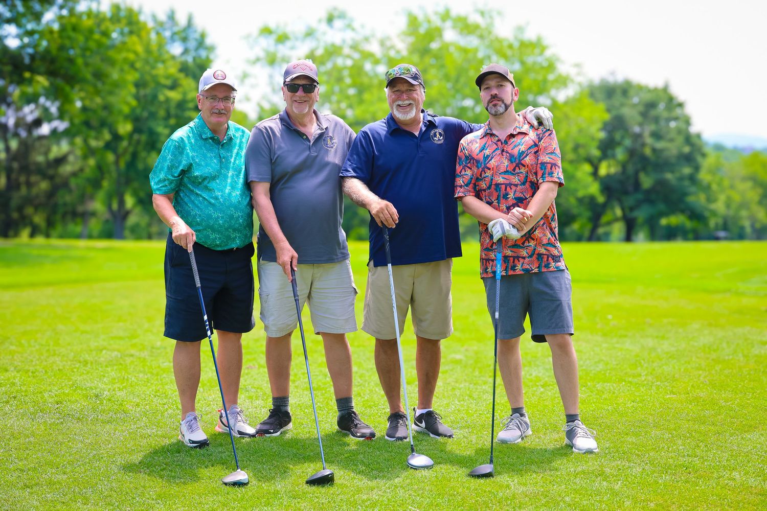 Four golfers stand together with their clubs on a sunny green golf course during a round of golf.