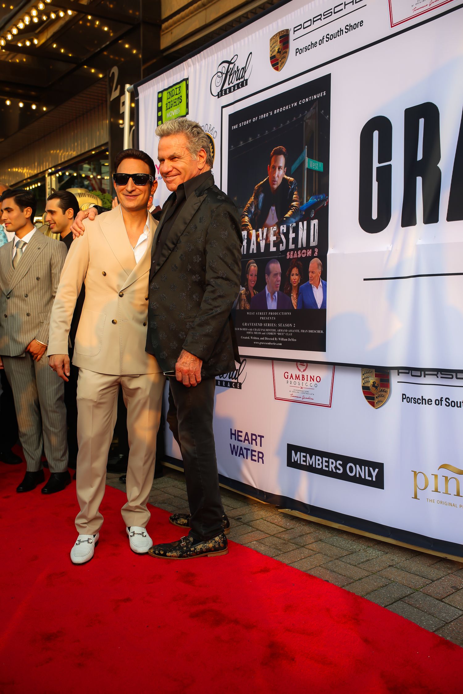 People stand on a red carpet at a formal event with illuminated signage and banners in the background.