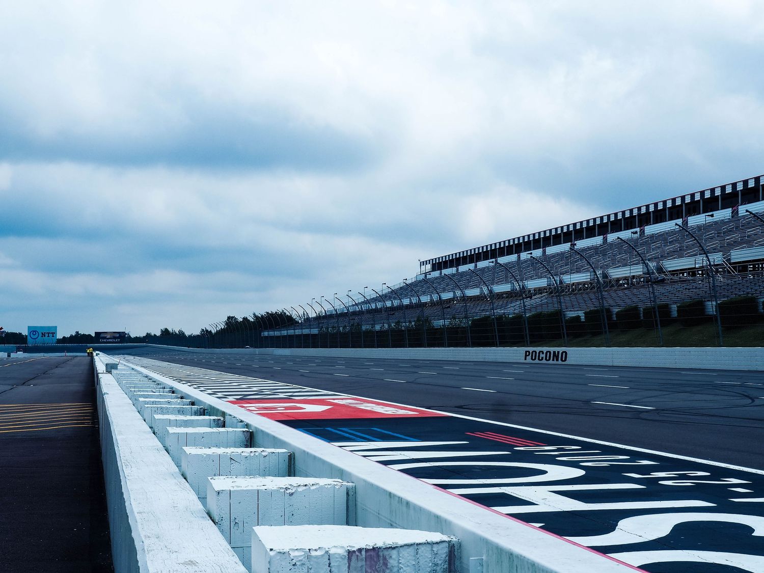 Wide angle shot of a racing track's start-finish line with pit lane wall and empty grandstands visible.