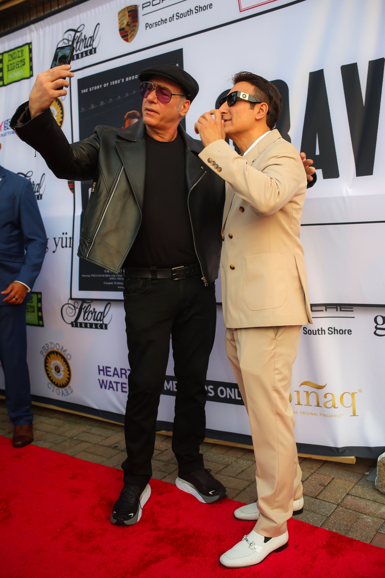 A person in a cream-colored suit and white shoes poses in various playful stances on a red carpet at an event.