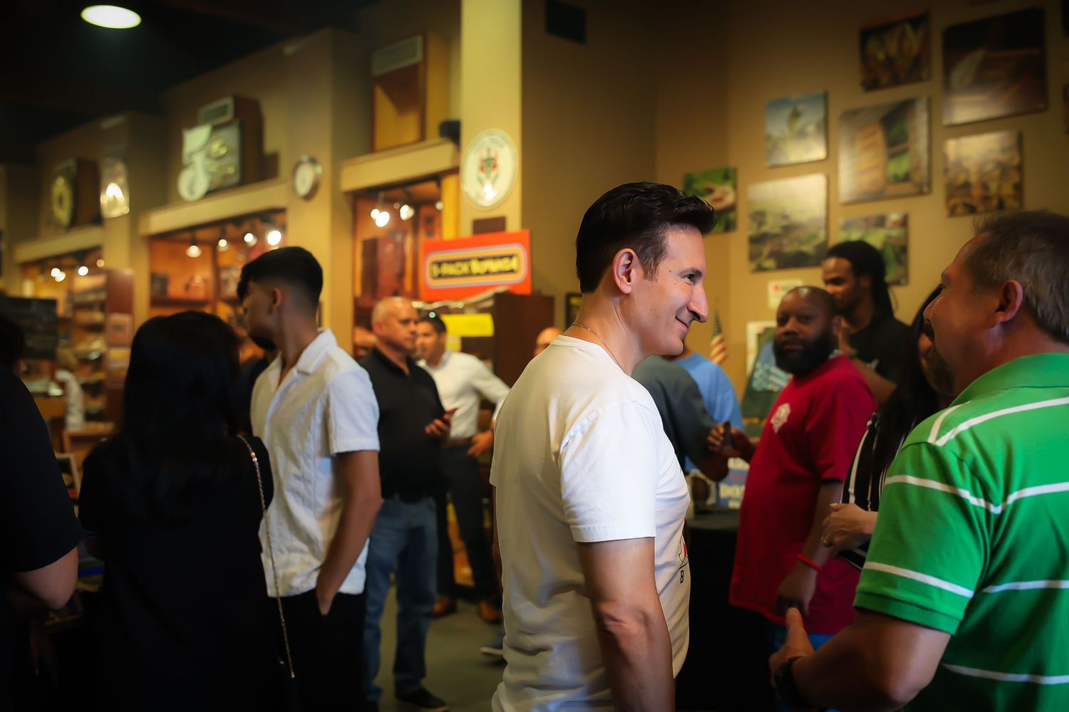 People waiting in line at a crowded restaurant with framed artwork on walls and warm lighting.