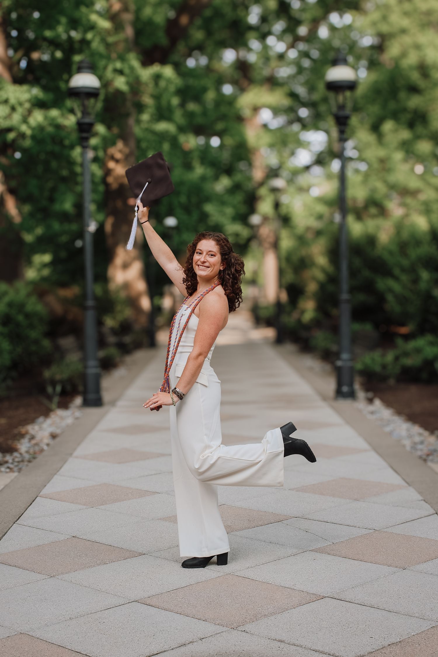 A person in a white dress dances and twirls joyfully on a patterned stone walkway surrounded by greenery.