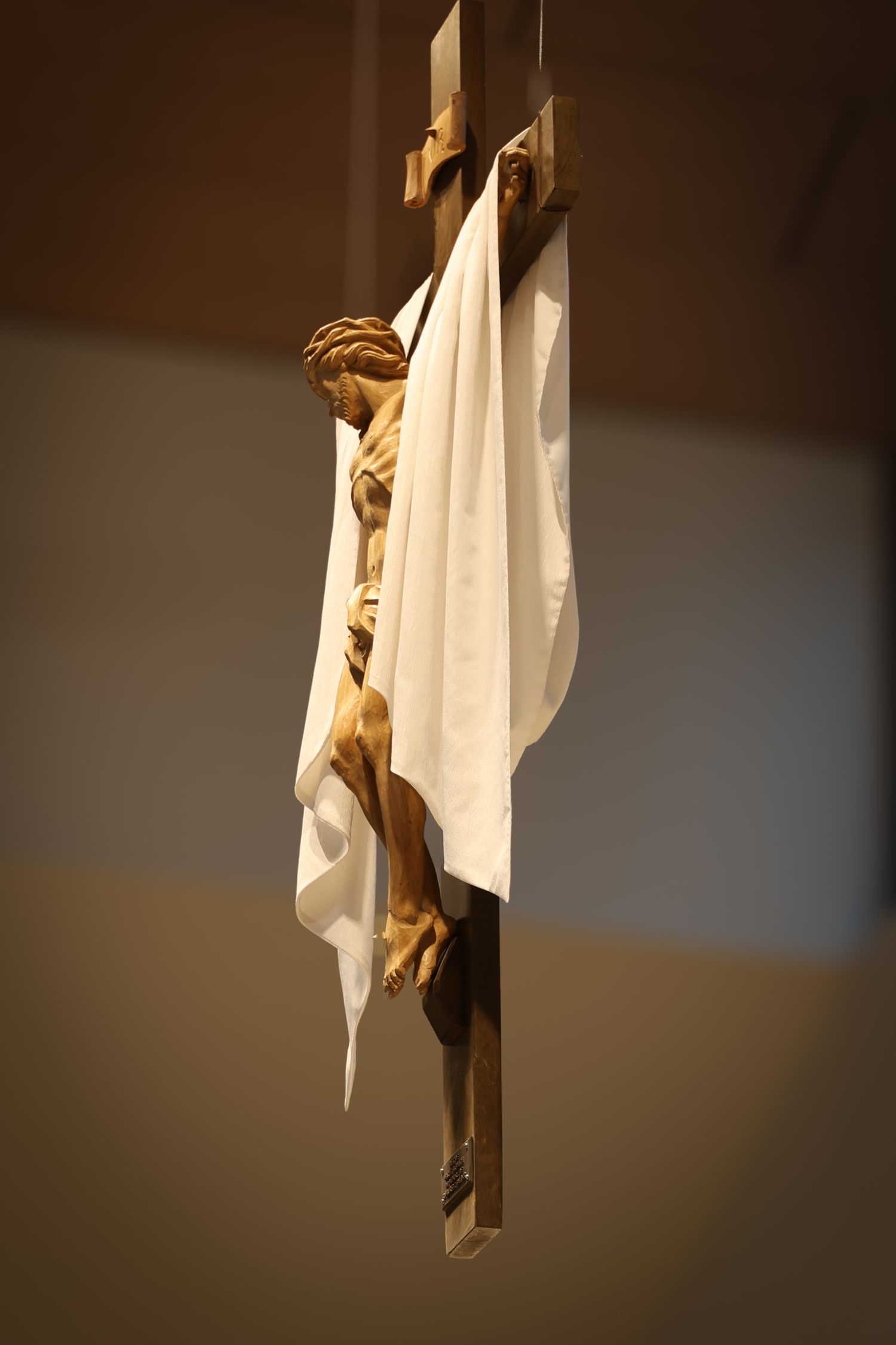 Crucifix with white cloth draped over it photographed in dramatic lighting against dark background.