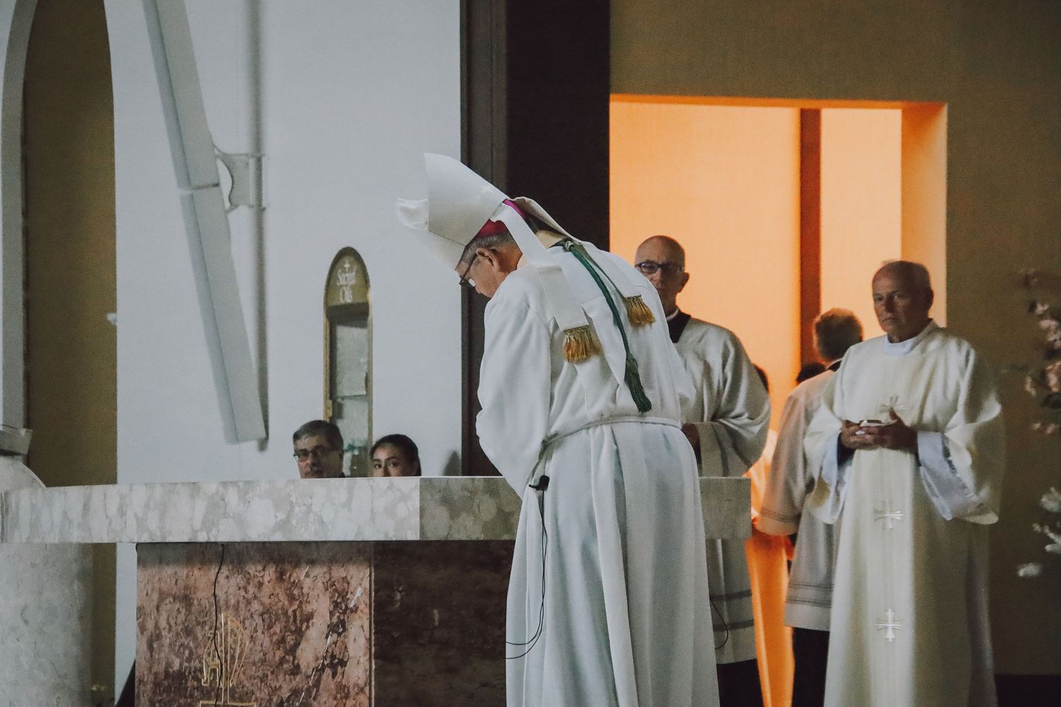 Religious figures in white robes stand in a church during a ceremonial service.
