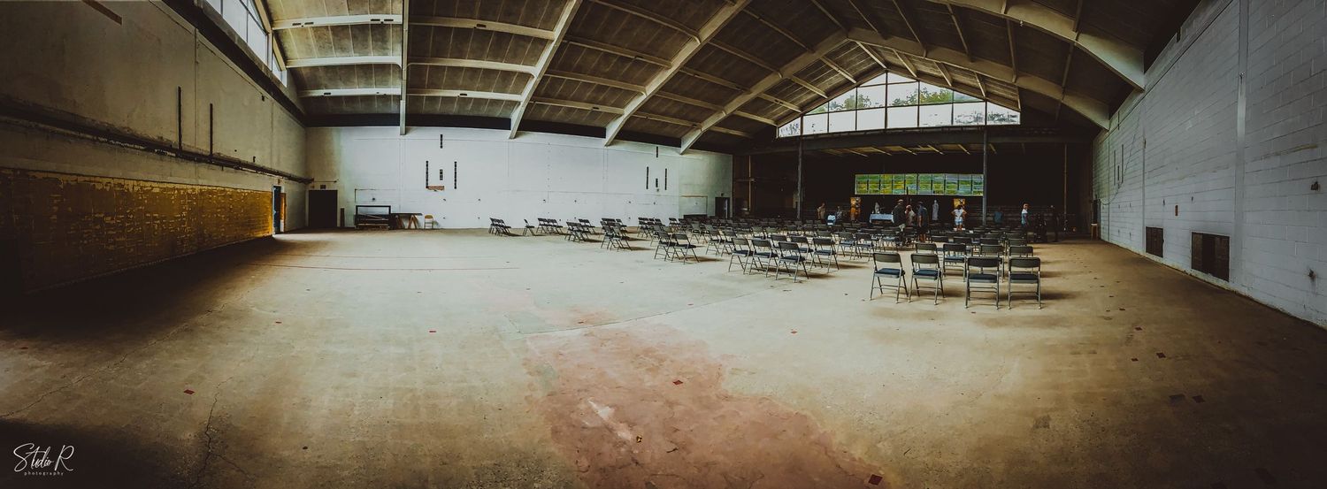 A panoramic view of an empty indoor gymnasium with wooden floors and folding chairs along the walls.