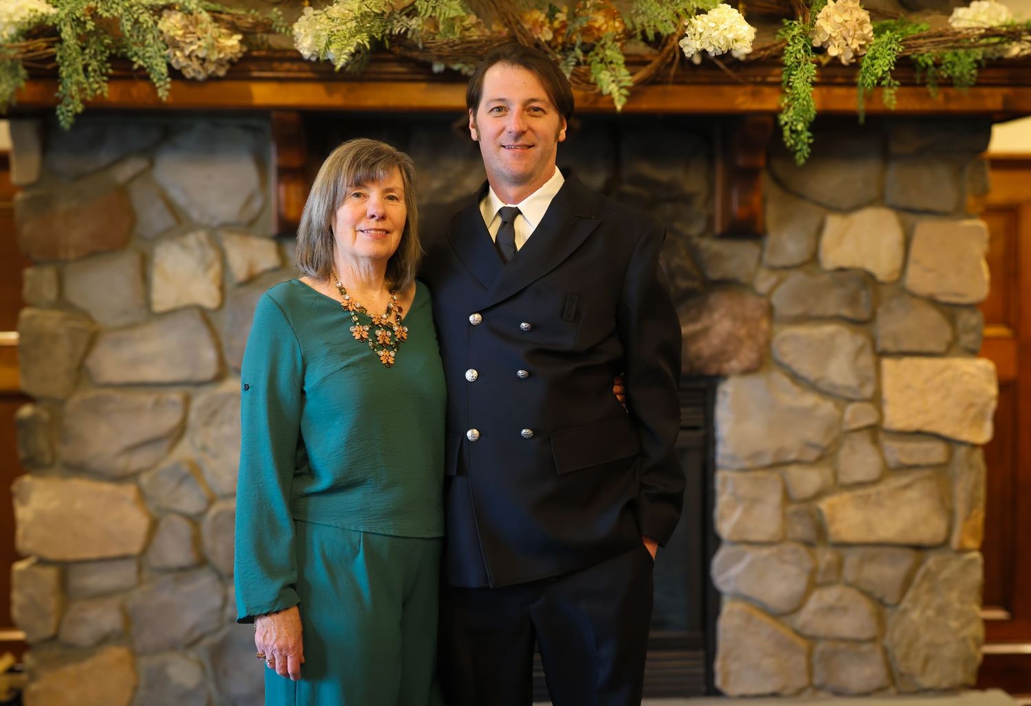 A couple poses together in front of a stone wall backdrop in a rustic indoor setting.