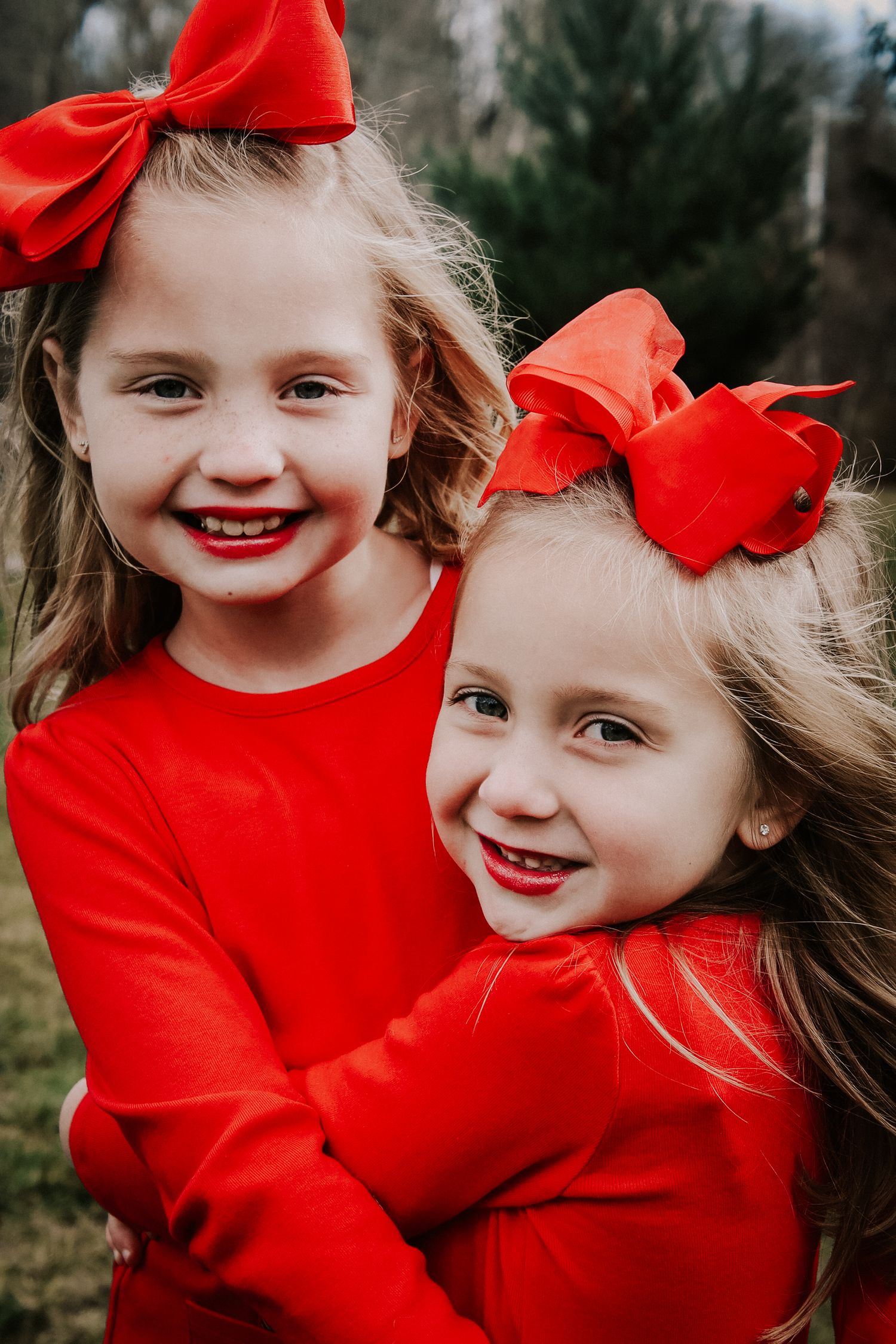 Children in bright red outfits and bows share joyful smiles while playing outdoors.
