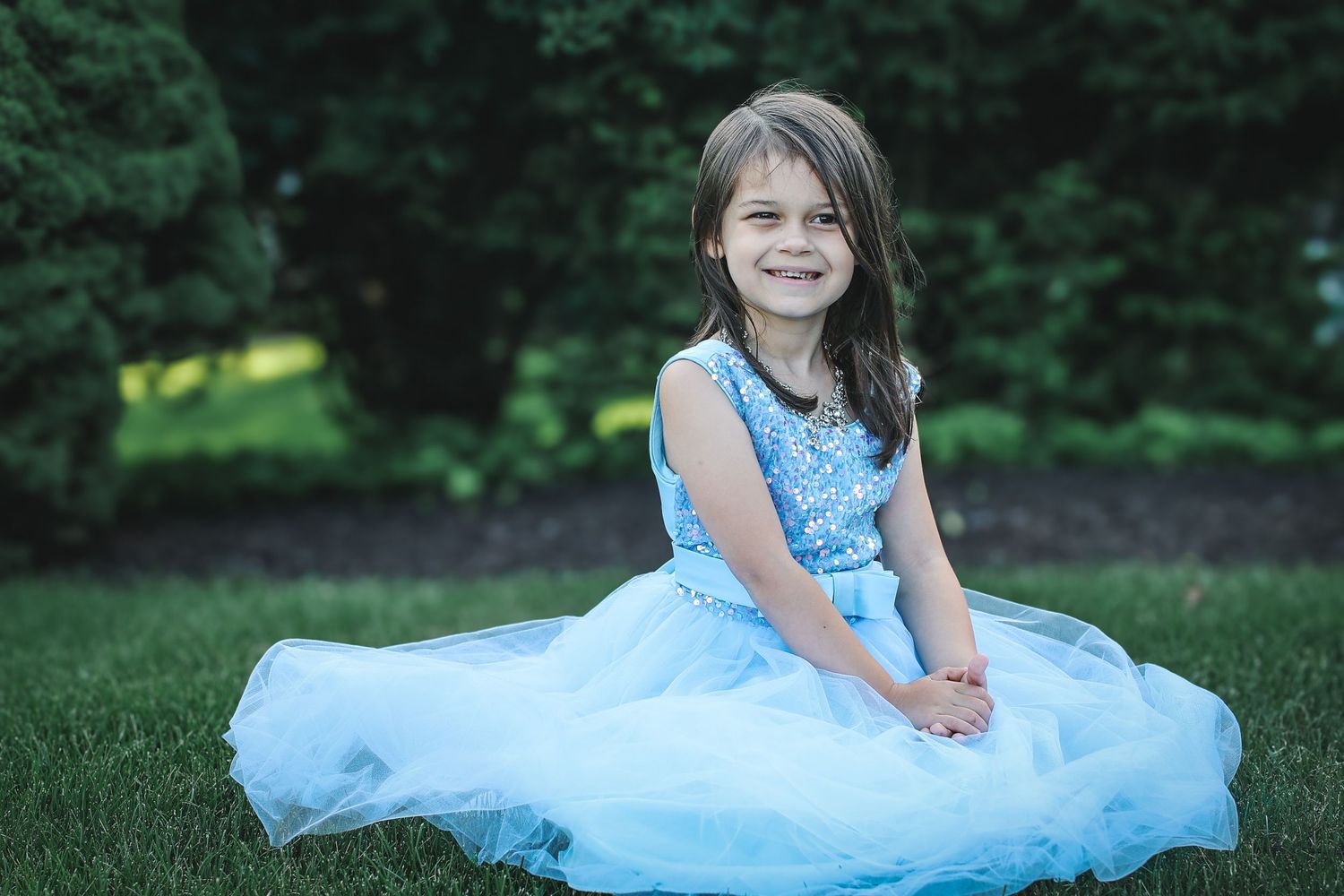 A series of photos showing someone in a light blue tulle dress sitting and posing in an outdoor garden setting.