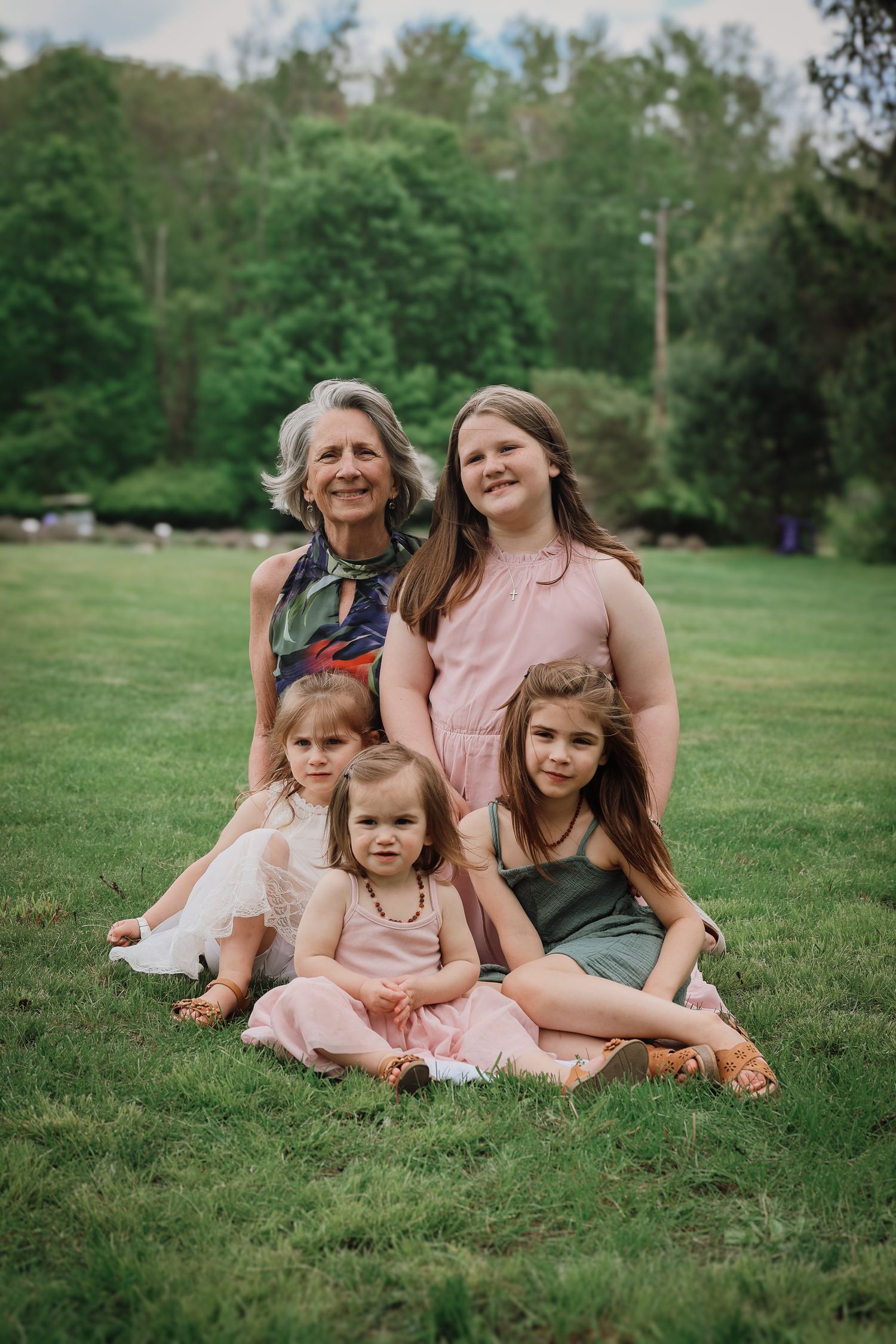 A family in coordinated pink outfits sits together on green grass during an outdoor photo session.