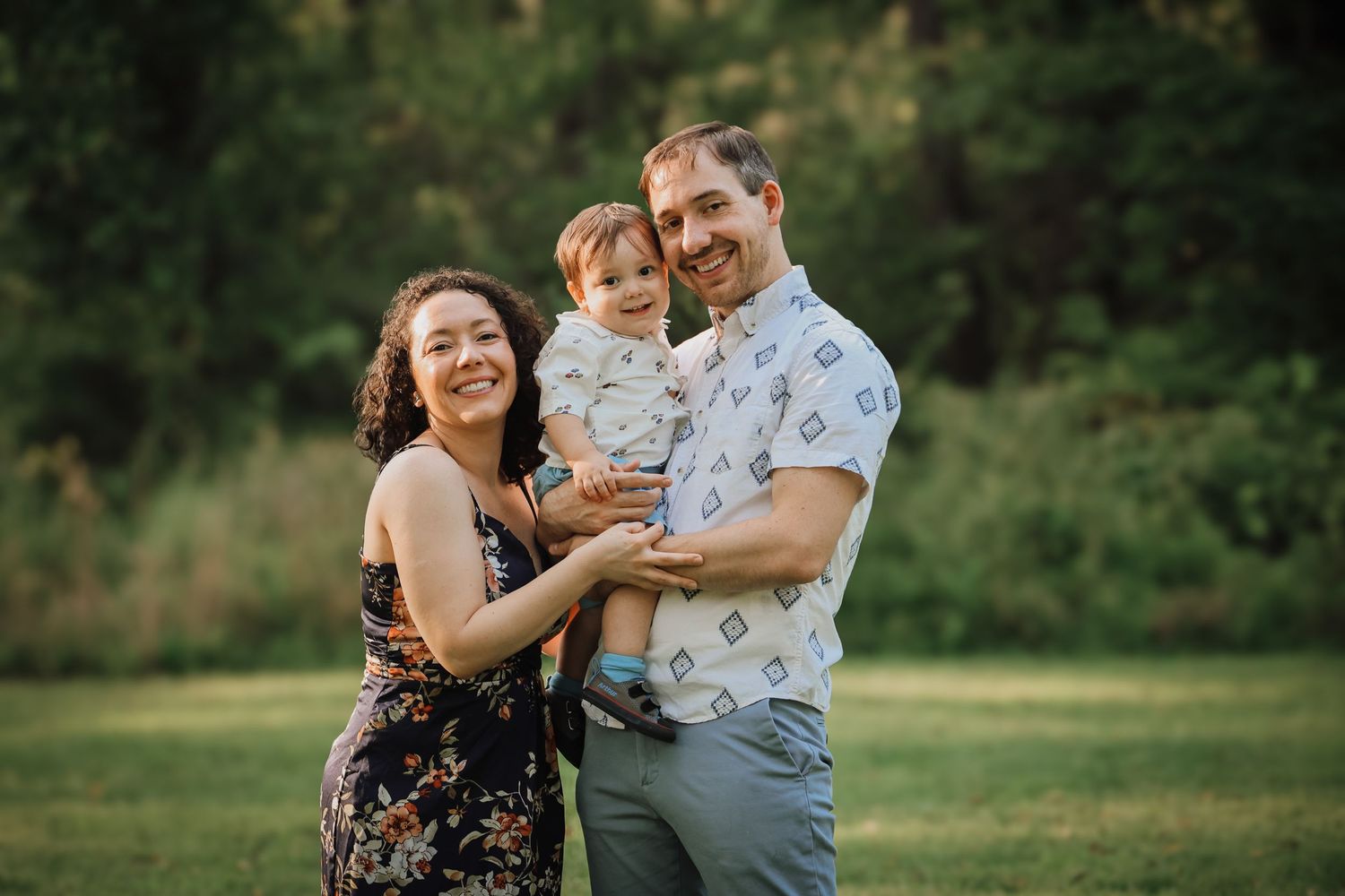 A family shares joyful moments together in a grassy outdoor setting during a summer photo session.