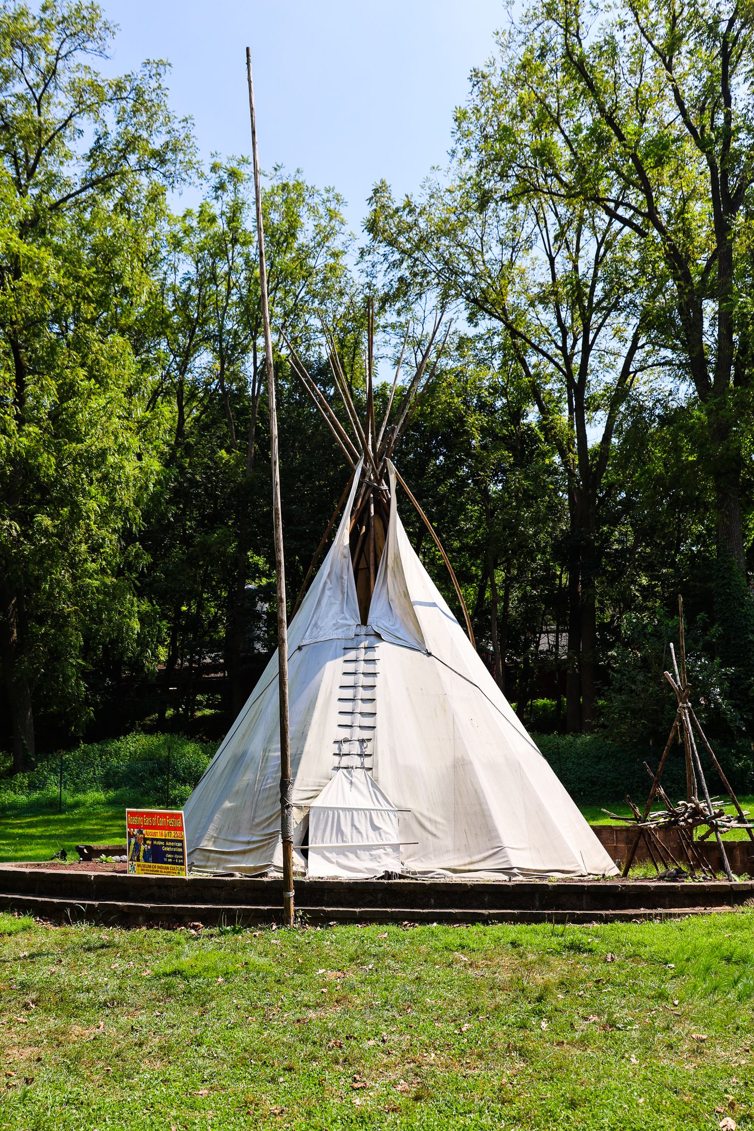 Traditional white teepees stand in a grassy clearing surrounded by green trees at a Native American cultural site.