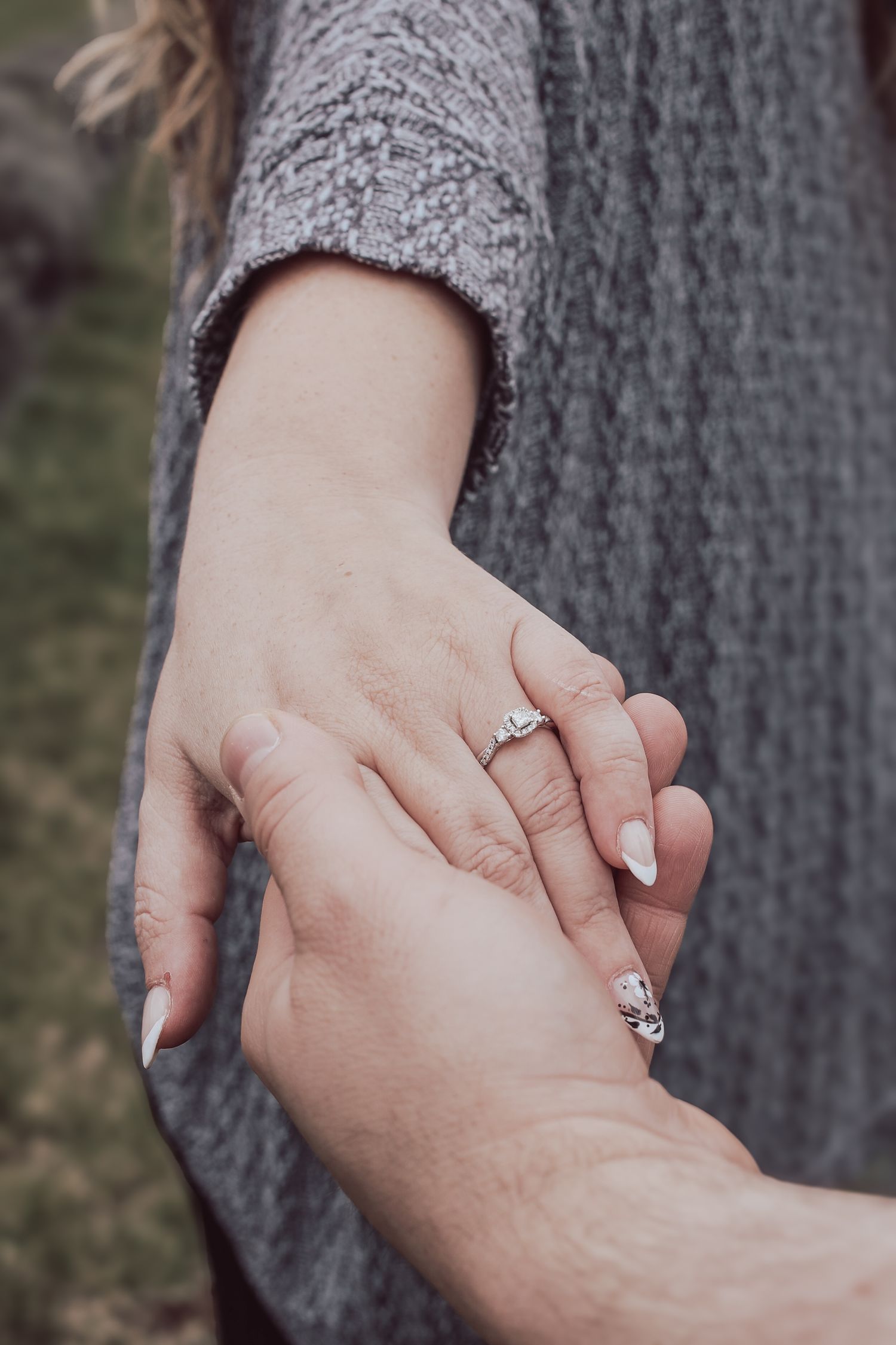 Close-up of two hands clasping together showing engagement rings in a romantic moment.