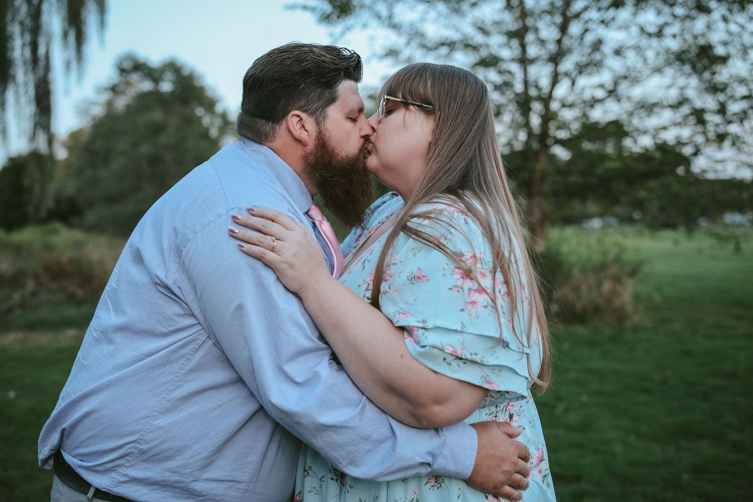 A couple shares romantic kisses in a grassy outdoor setting during a photo session.