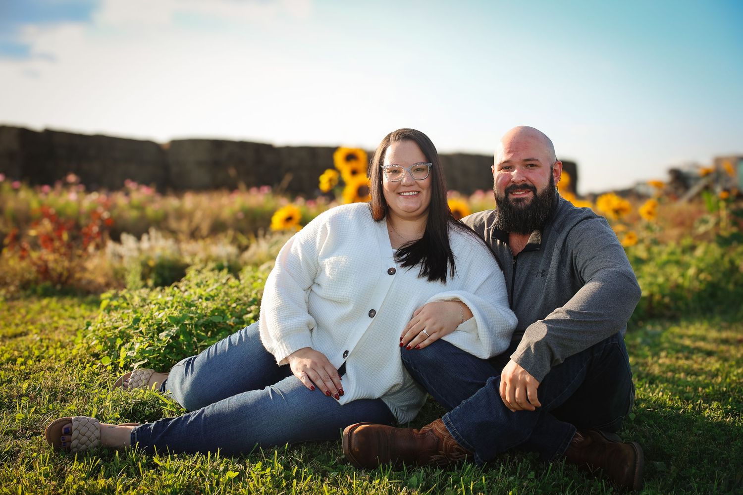 Couple sharing intimate moments while laying in a sunlit meadow with yellow wildflowers during golden hour.