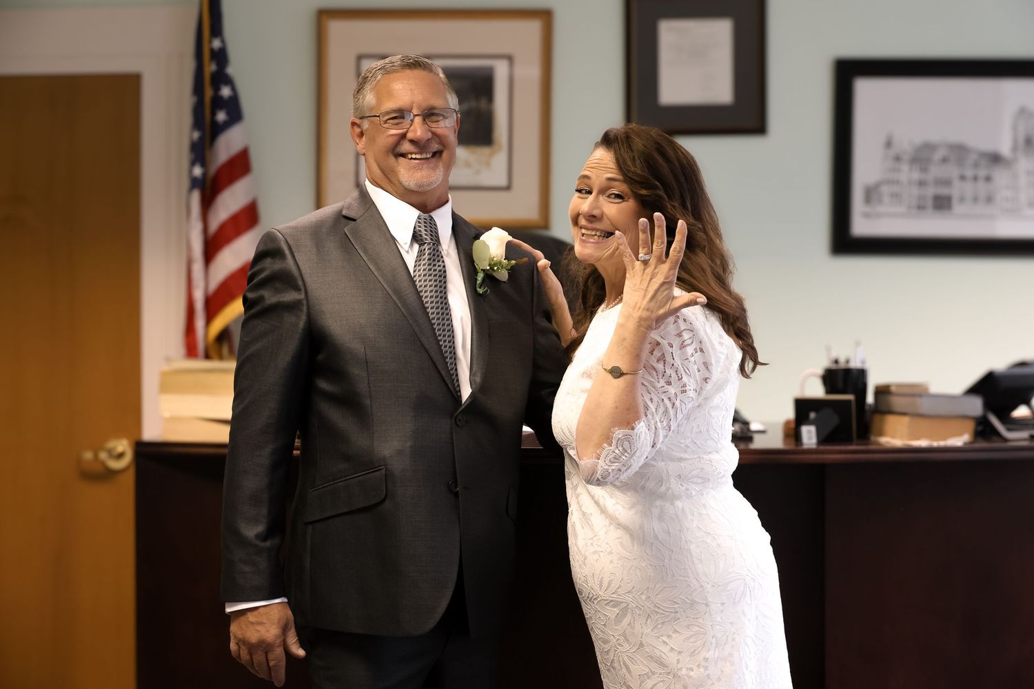 A happy couple shares a joyful moment during their courthouse wedding ceremony with an American flag in the background.