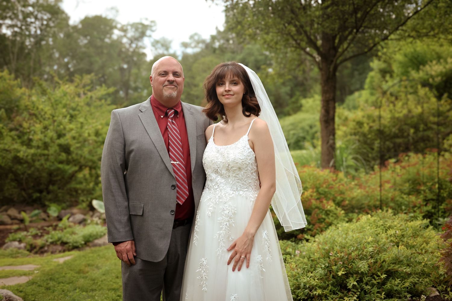 A couple poses together in a lush garden setting during a wedding celebration with greenery in the background.