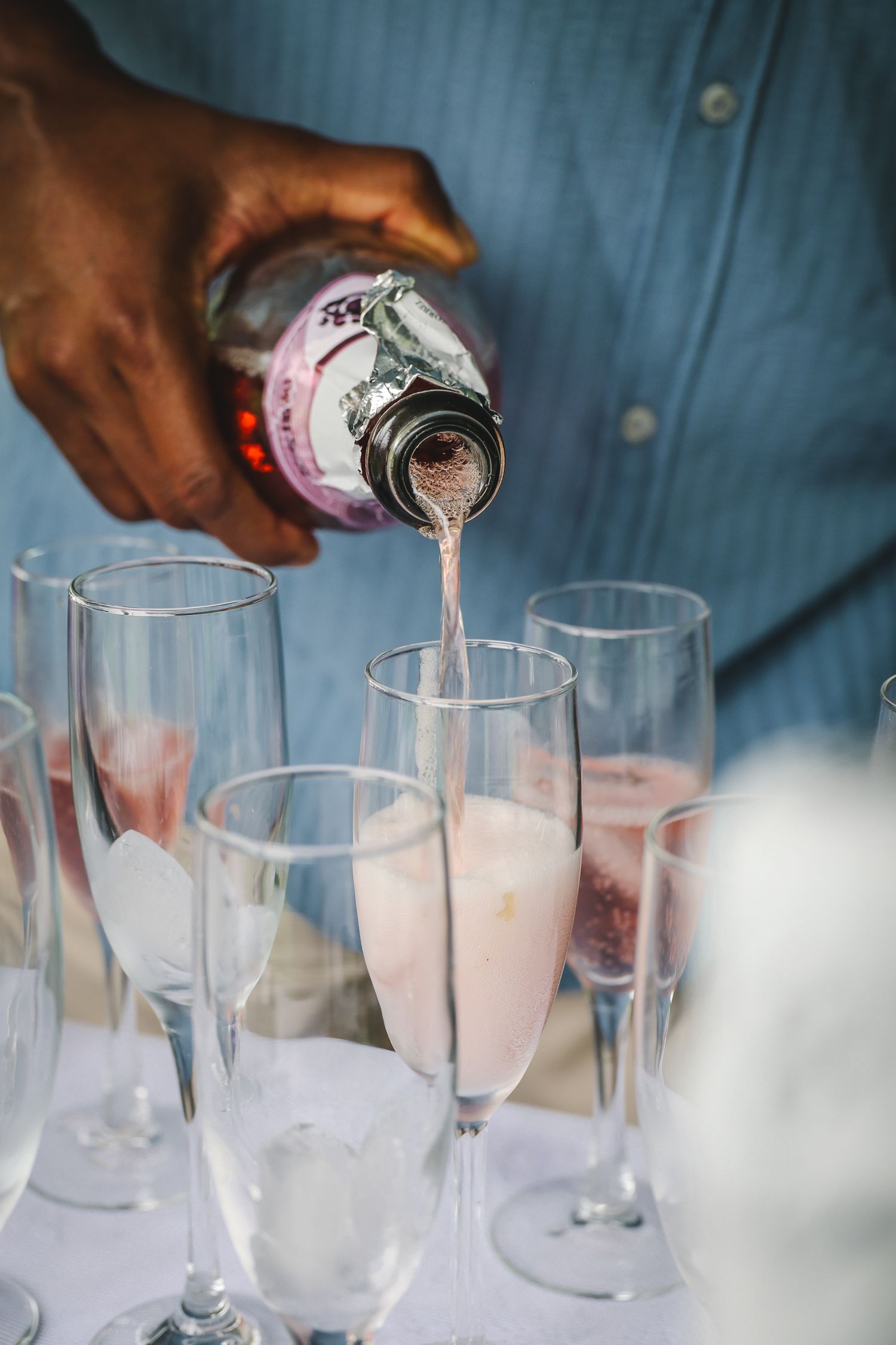Pink cocktails being poured into champagne flutes at a special event with a blue background.