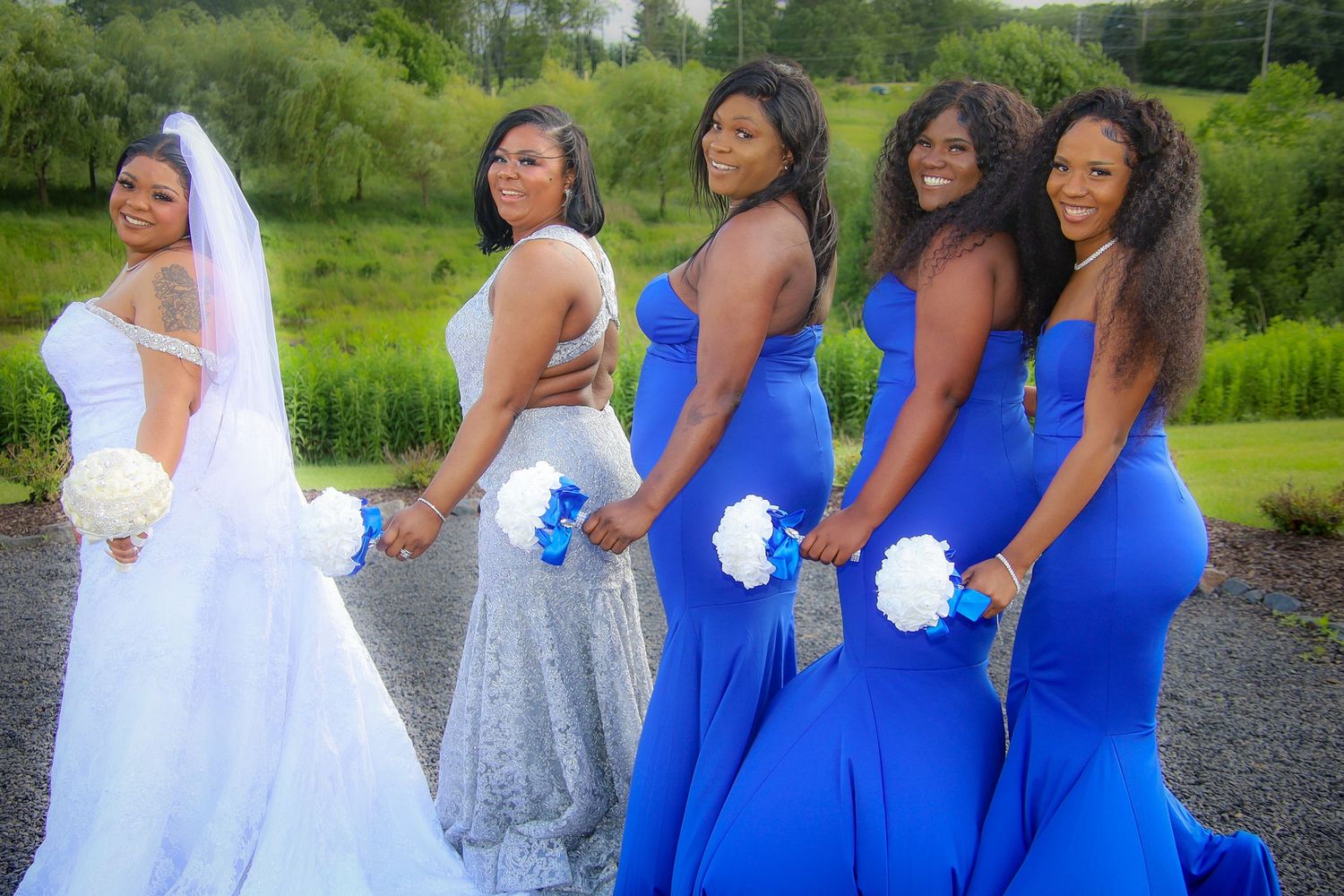 Wedding party in white and royal blue dresses pose together outdoors in a garden setting.
