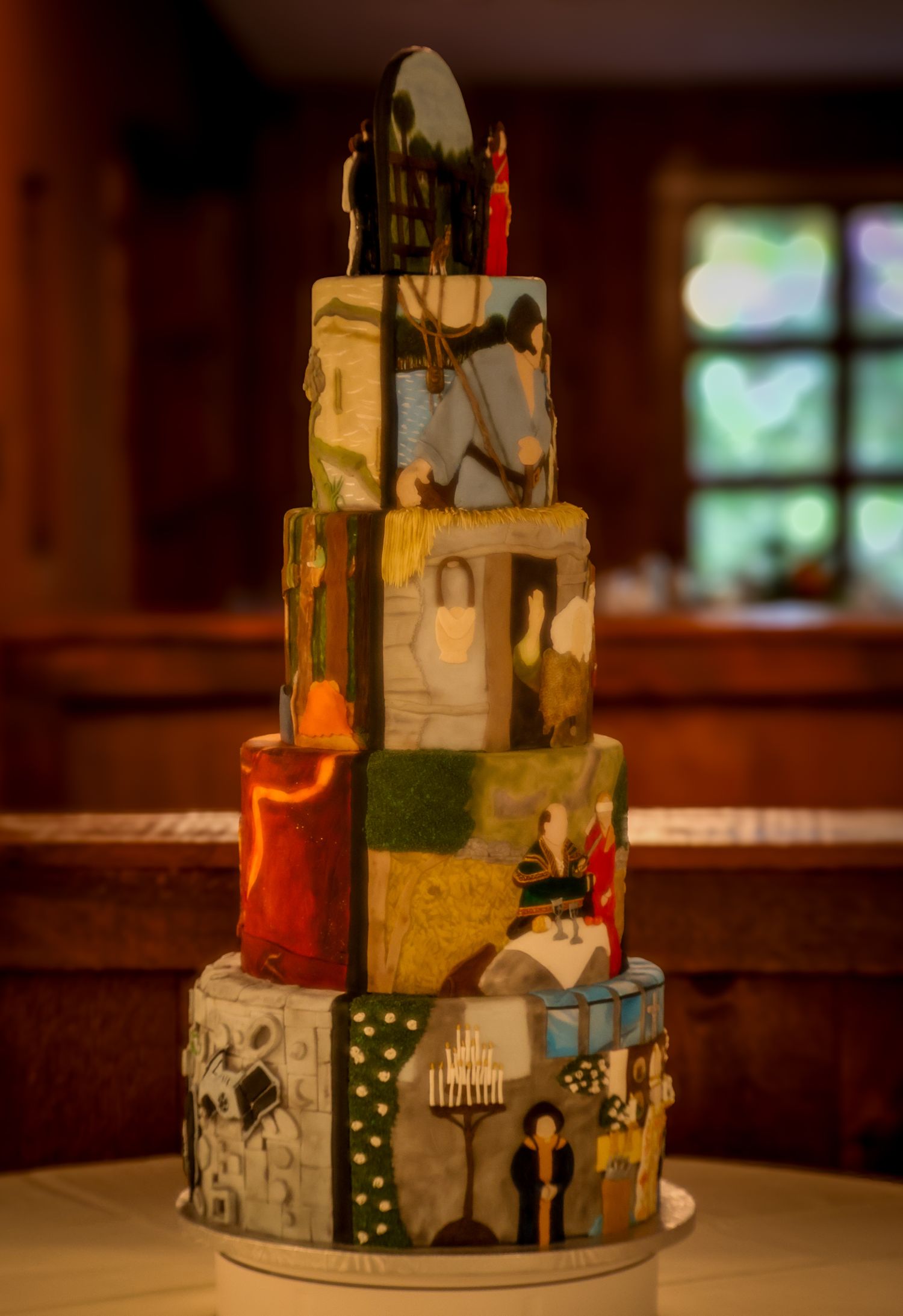 A tiered wedding cake decorated with black and white designs and illustrations sits on a wooden table in warm lighting.