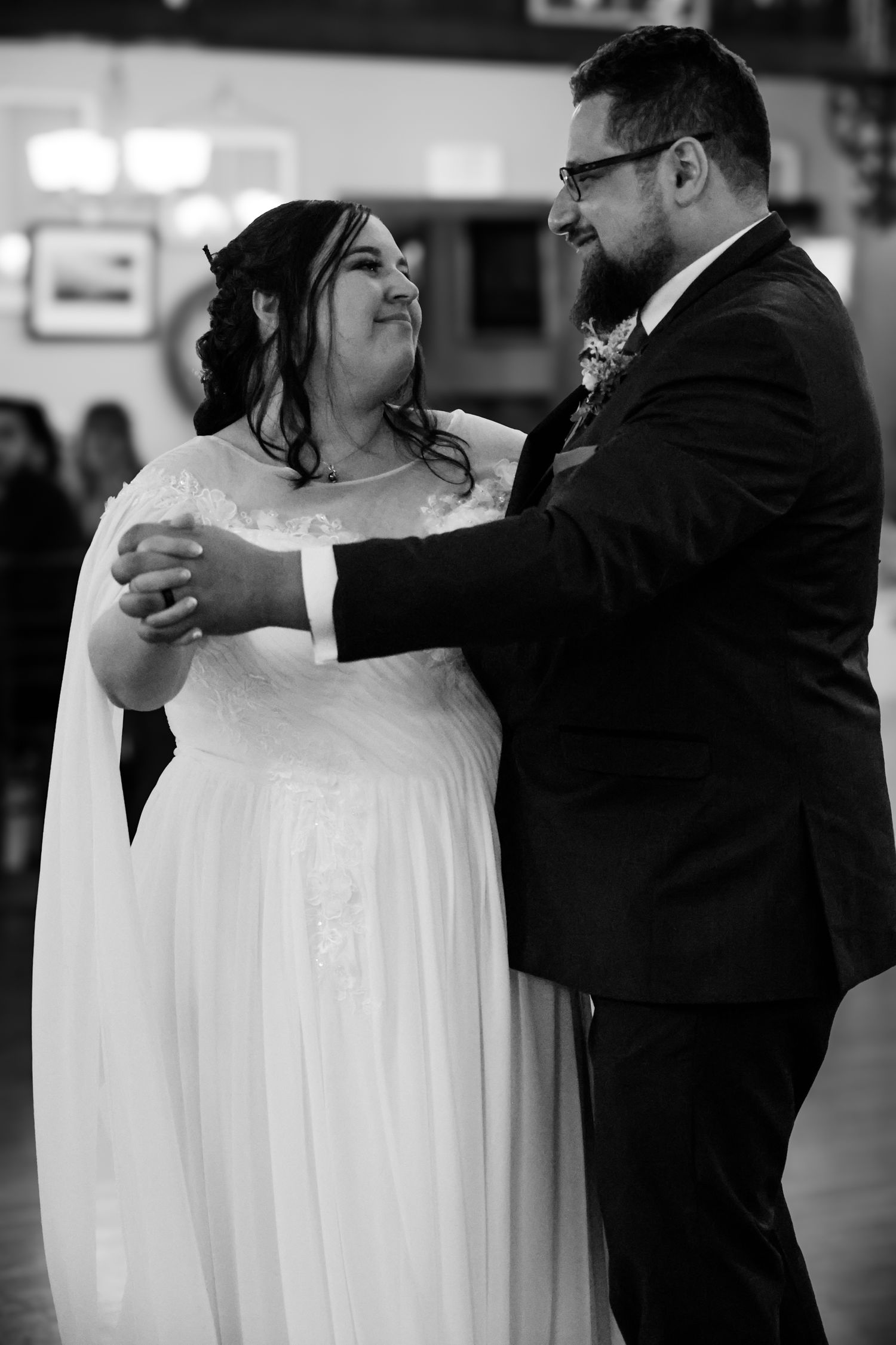 A couple shares their first dance at a wedding reception, with the bride in a flowing white gown and groom in black suit.