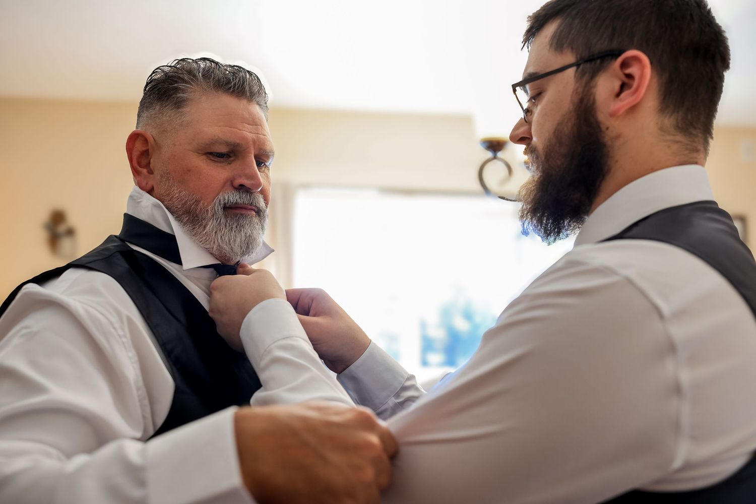 A person helps another adjust a white dress shirt collar and tie in a formal getting-ready sequence.
