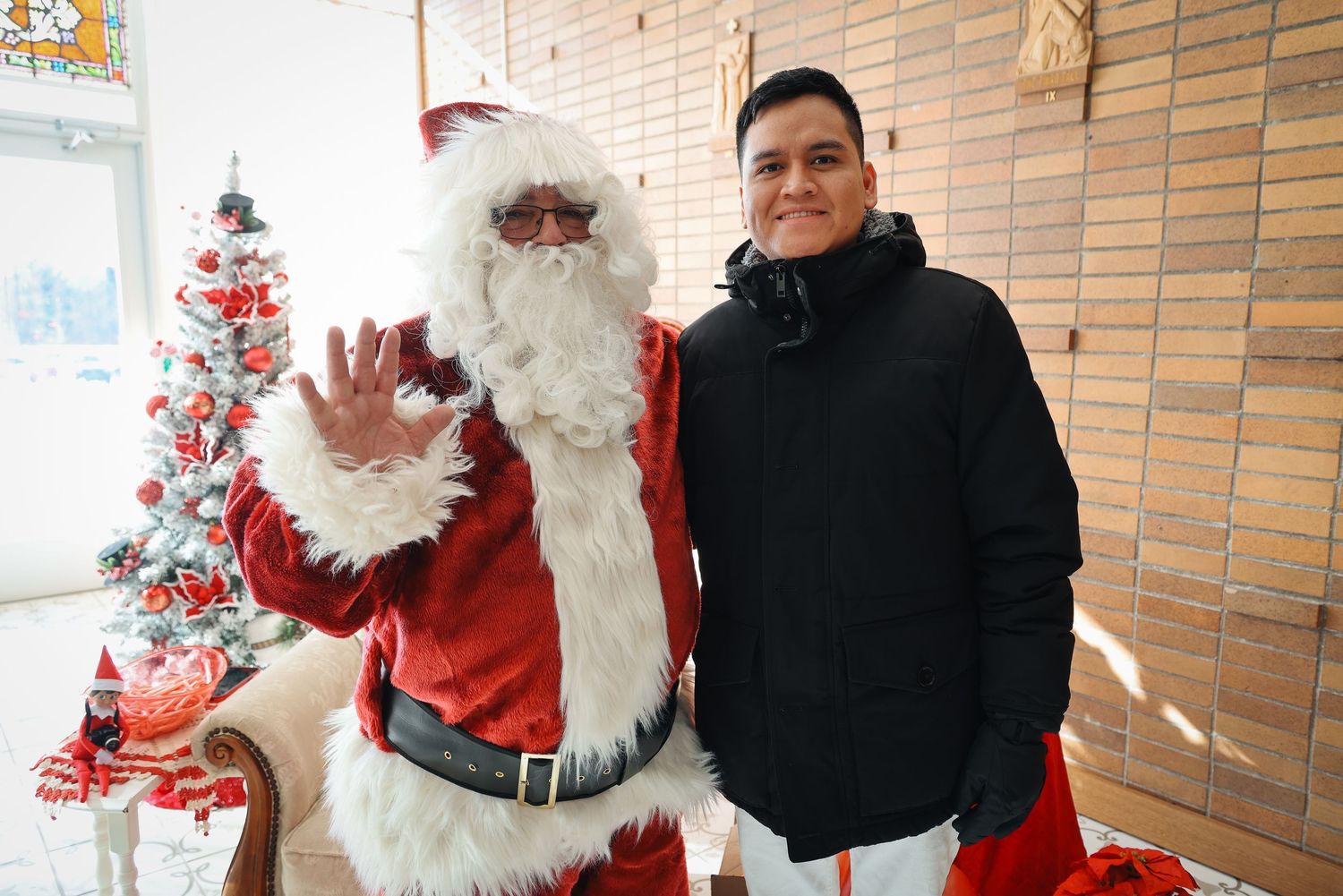 A group of people pose with Santa Claus in a brick-walled room during a holiday event.