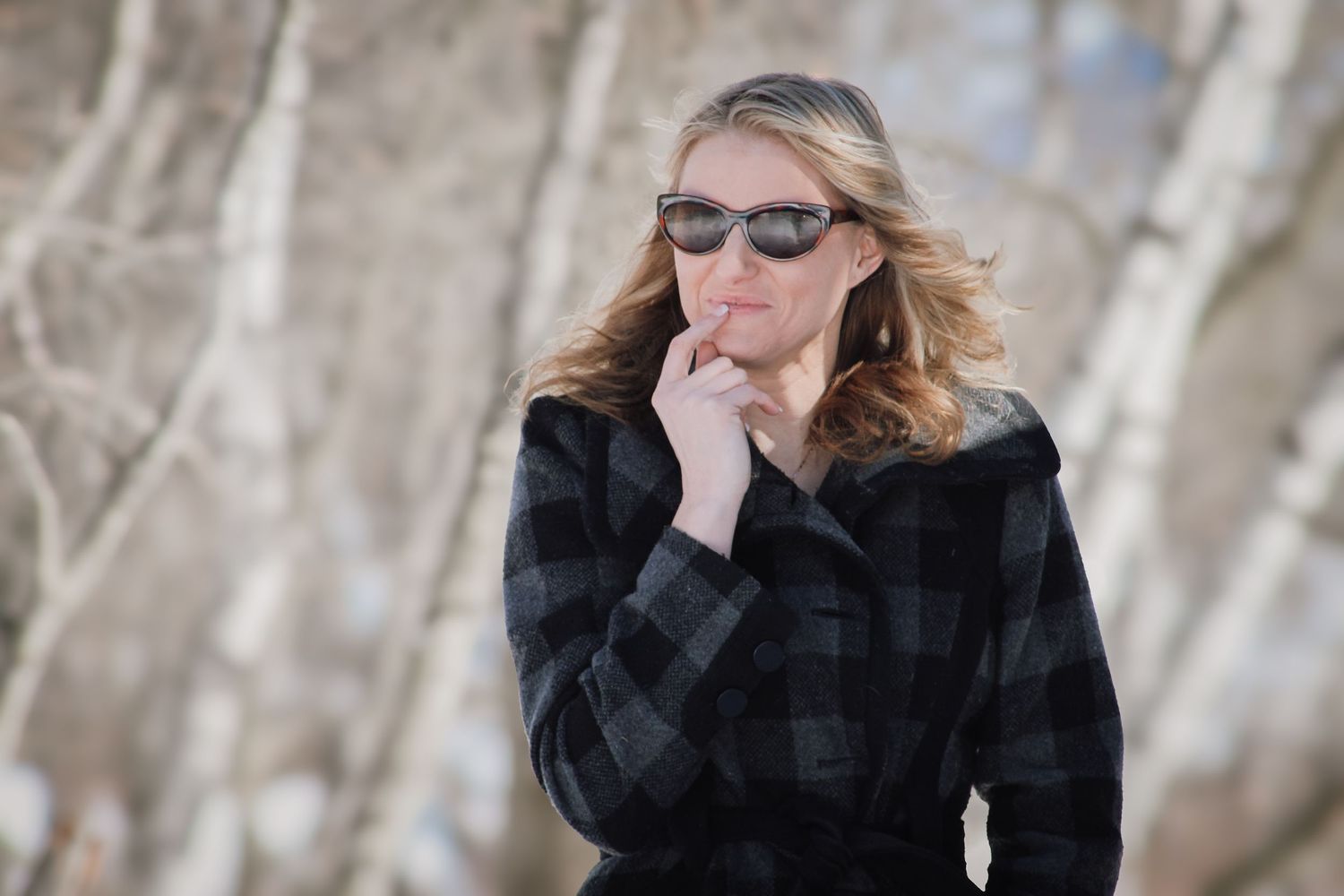 A person in a black coat plays harmonica outdoors in winter with bare trees in the background.