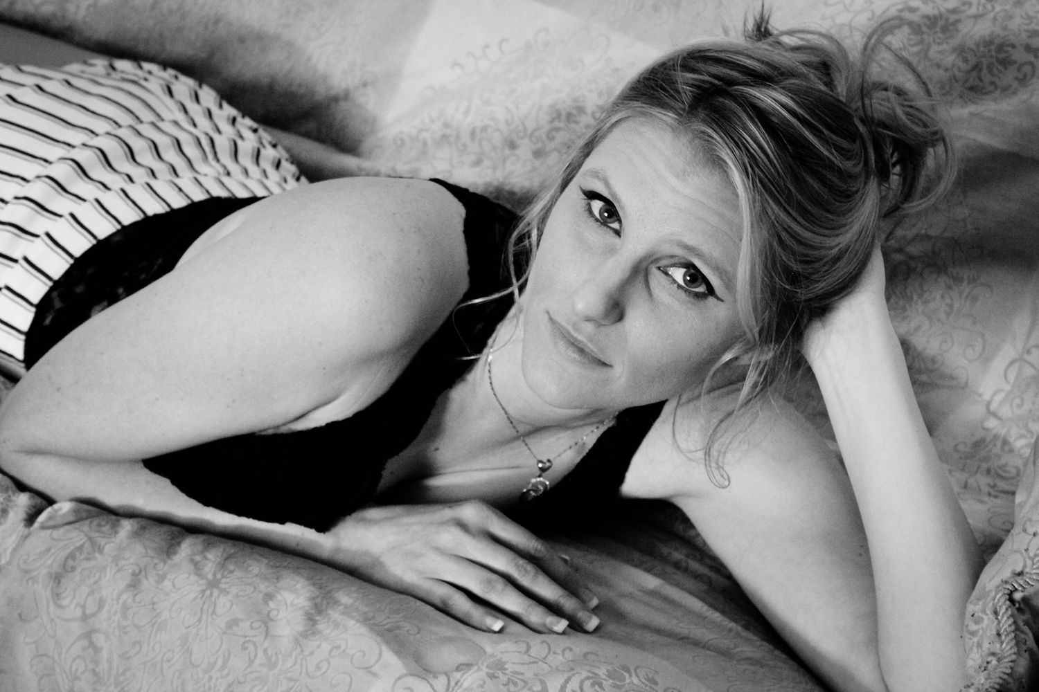 Black and white portrait of a woman lying down in casual pose on soft fabric, looking directly at camera.