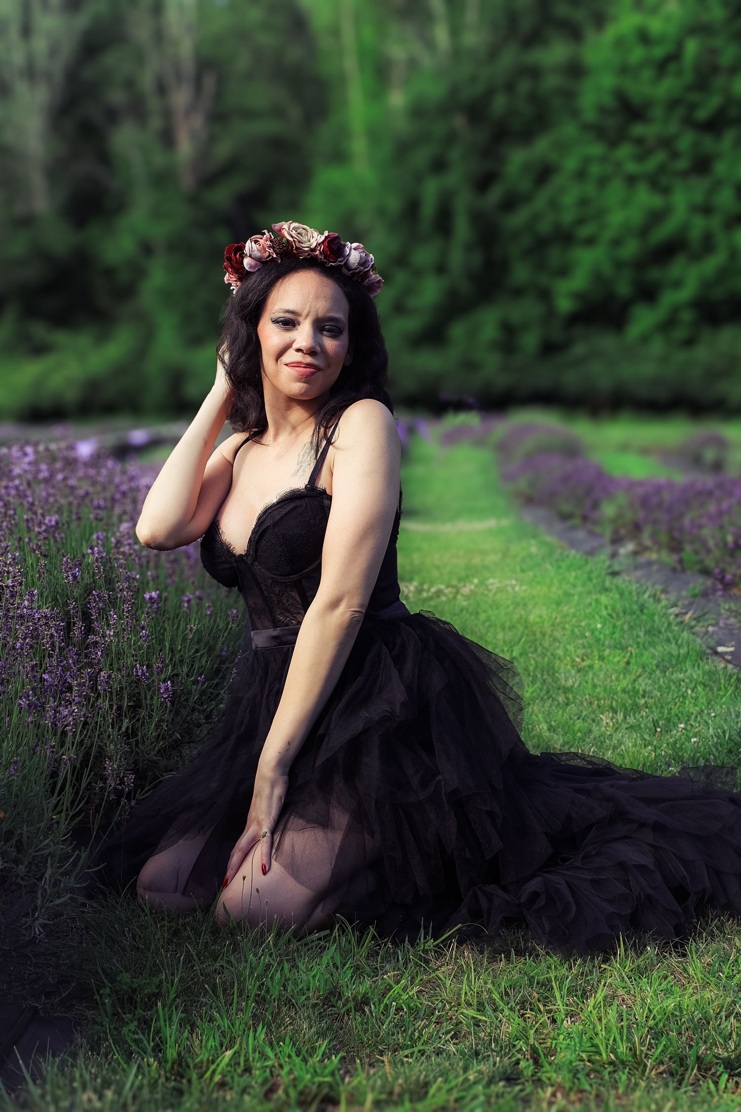 A person in a black tulle gown poses gracefully among blooming lavender fields on a lush green lawn.
