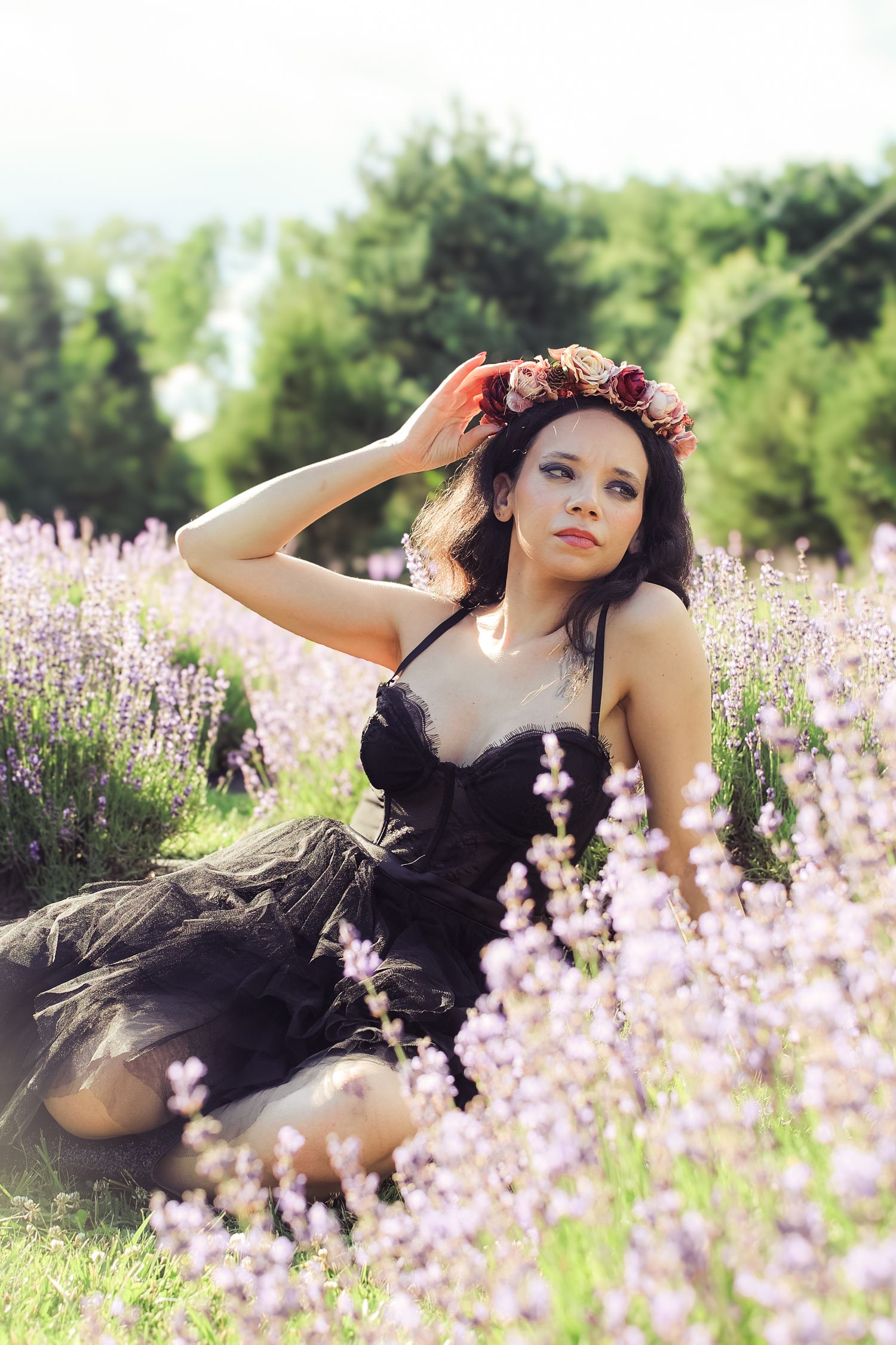 Person in black dress lying in field of purple wildflowers on sunny summer day.