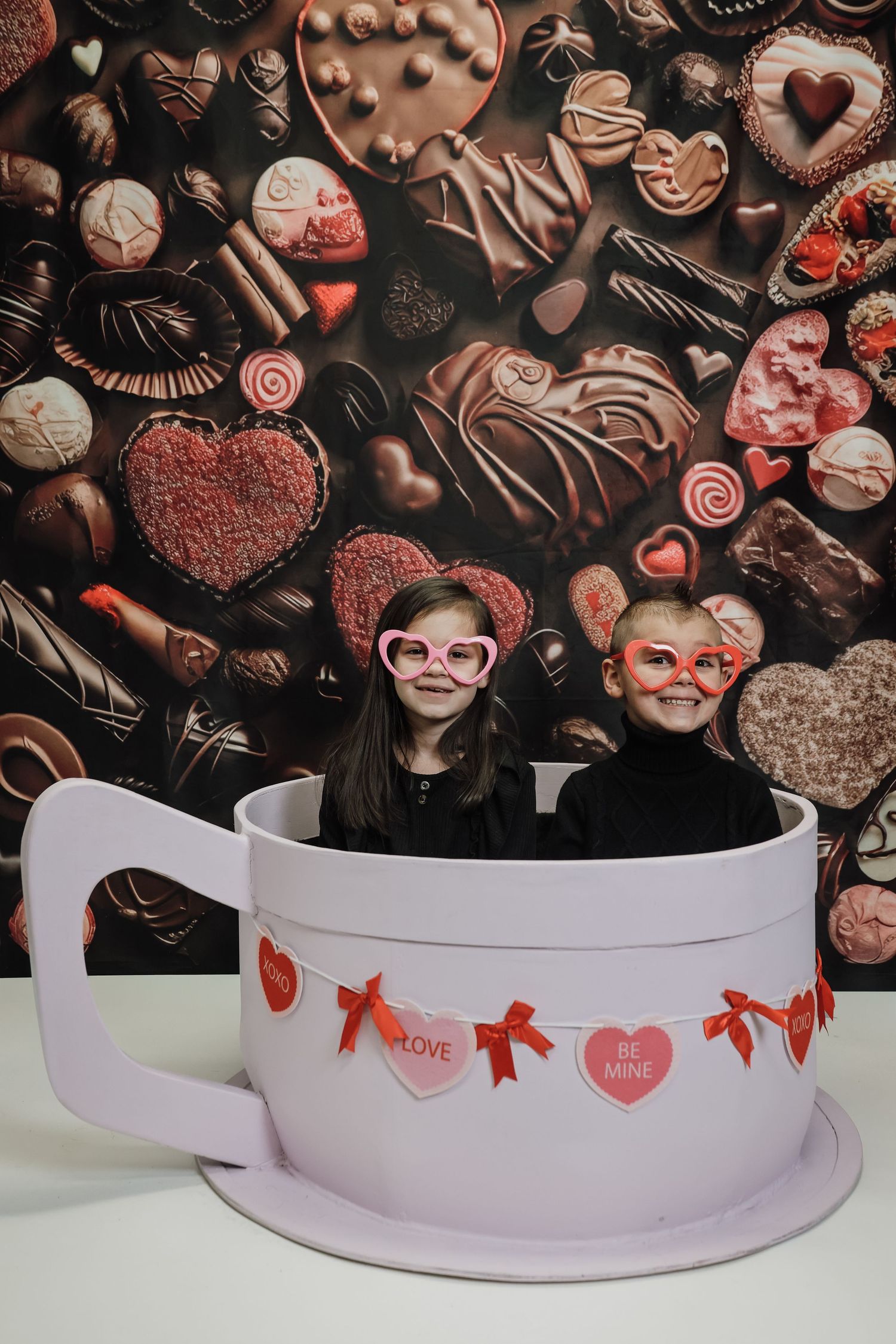 Dark chocolate truffles and heart-shaped candies arranged with red ribbons and Valentine's decorations on a curved white surface.
