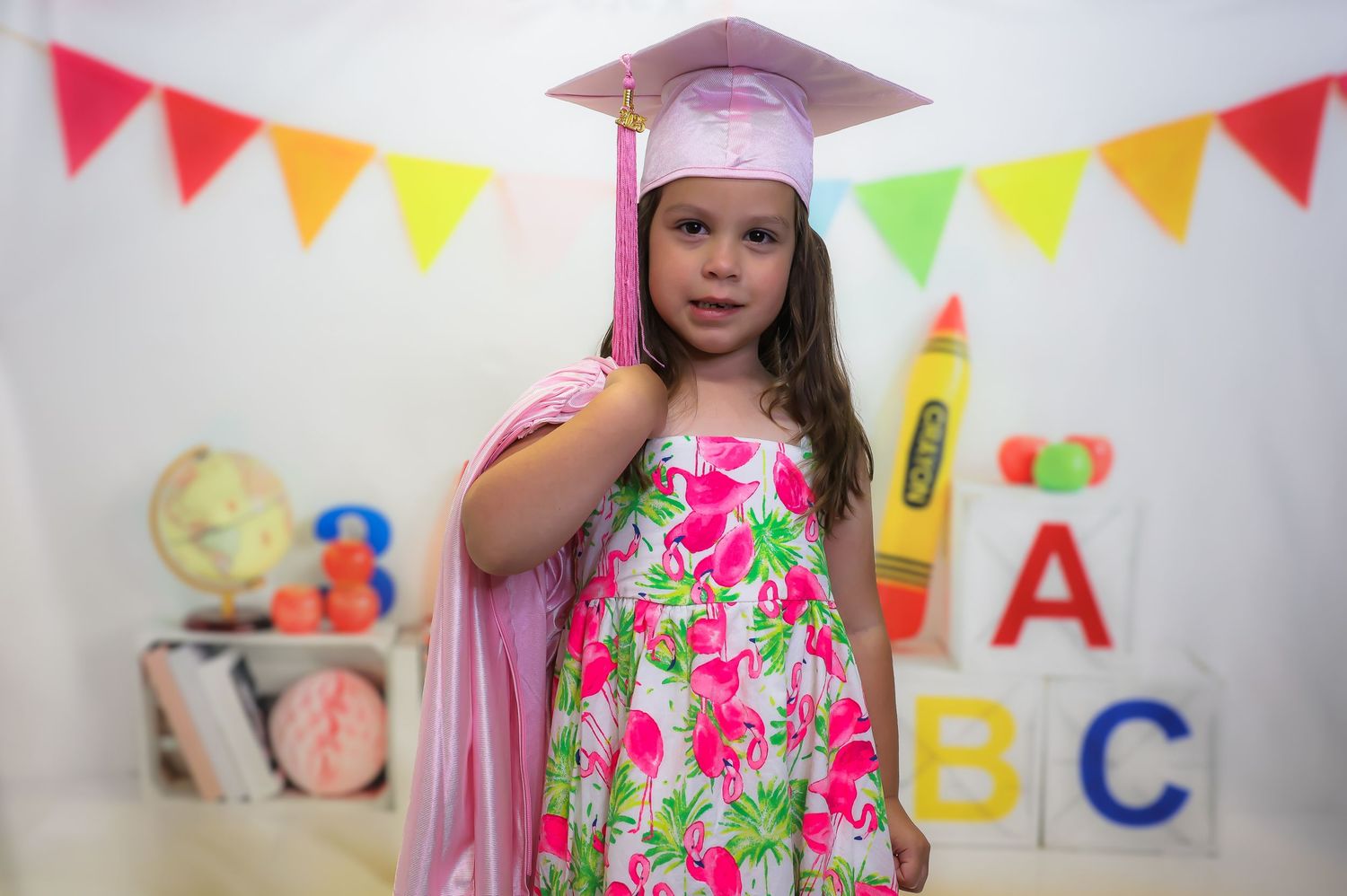 Colorful party scene with pink graduation cap, festive bunting flags, and ABC decorations against white background.