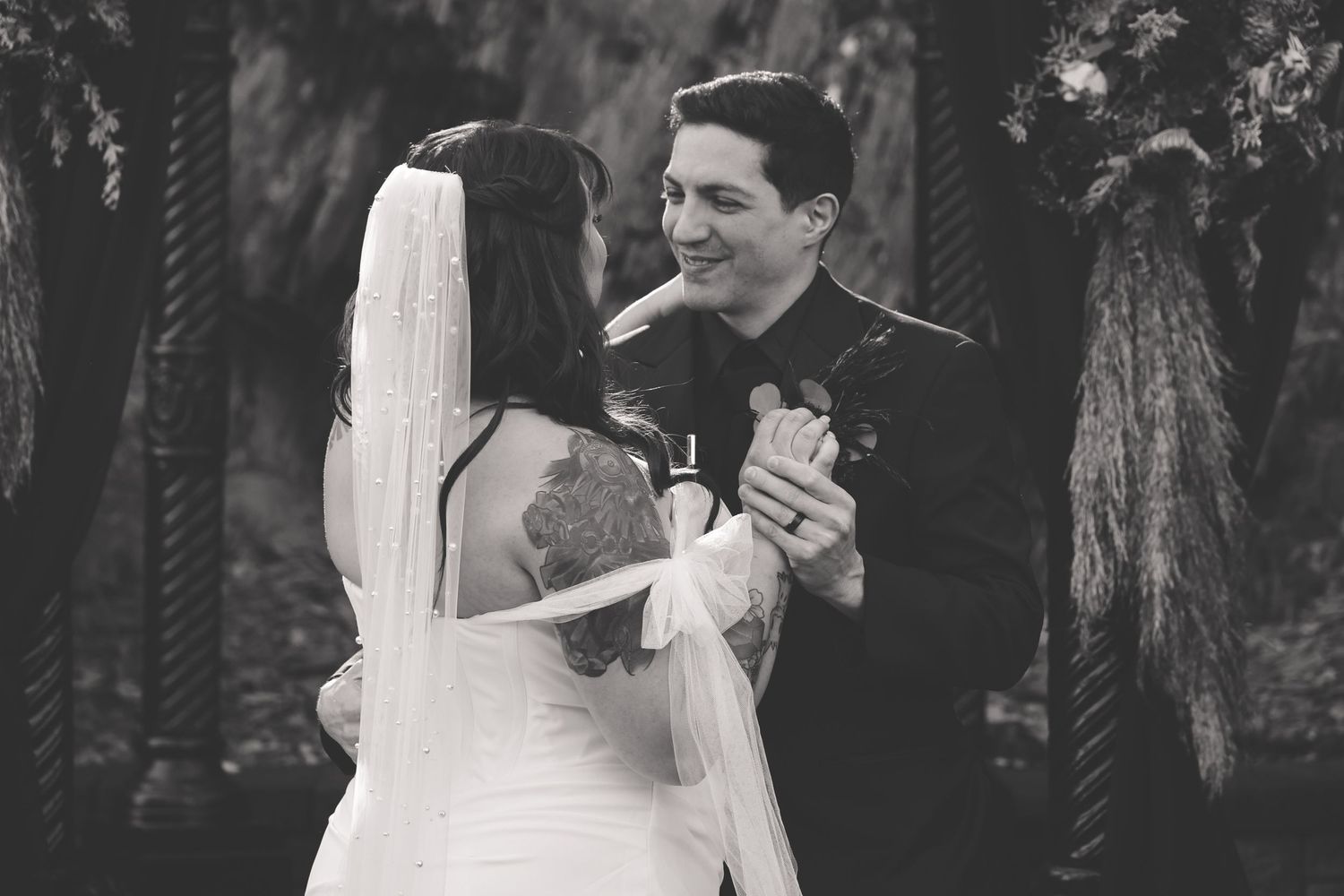 A black and white photo of a couple sharing their first dance at a wedding ceremony in a garden setting.