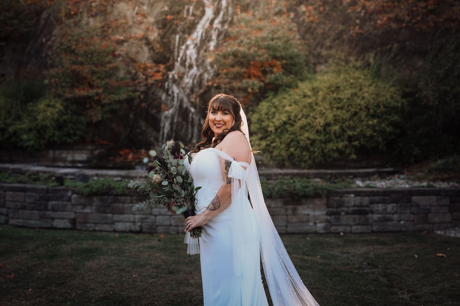 A couple in wedding attire embraces by a serene lake during an autumn day.