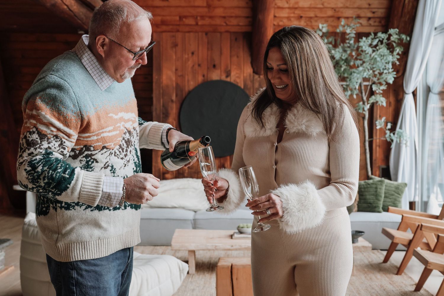Two people in cozy sweaters share coffee together in a rustic cabin setting with brick walls and natural light.