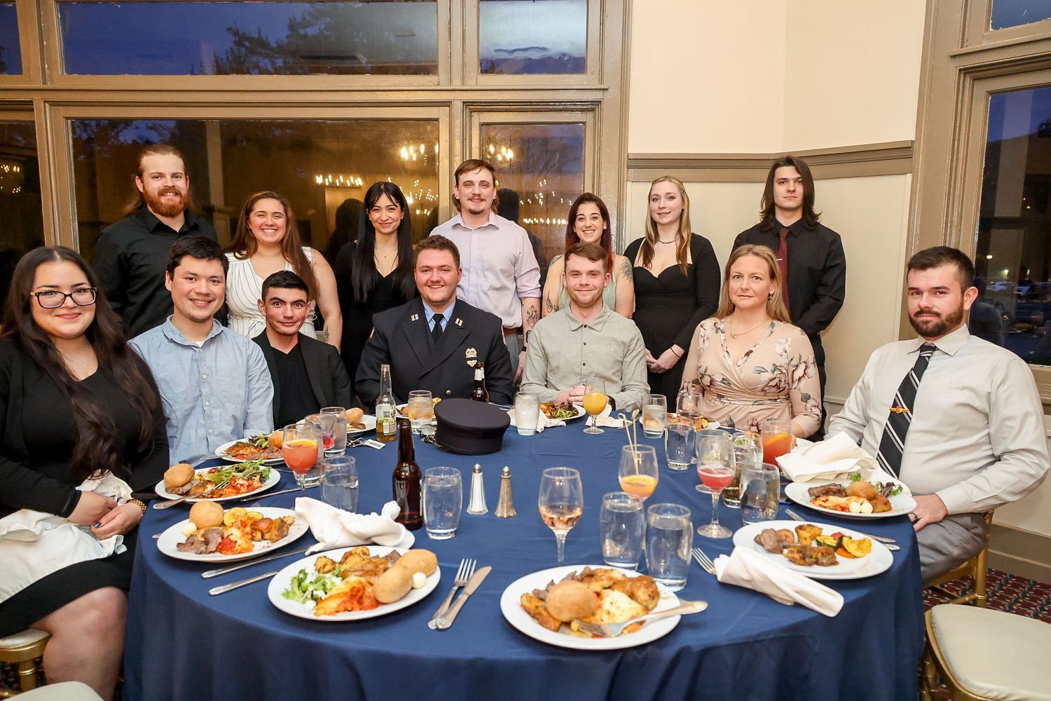 Group of professionals dining at a formal banquet table with blue tablecloth, food, and drinks in an elegant venue.