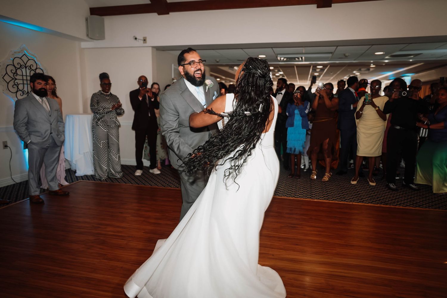 Bride and groom share their first dance at wedding reception, surrounded by guests in formal attire.