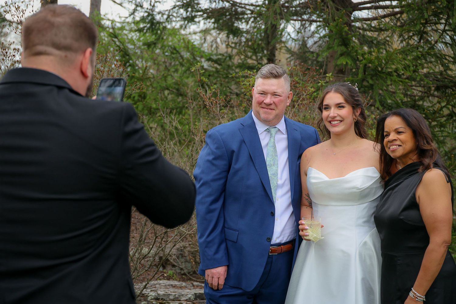 Bride and groom posing for a photo with a guest at an outdoor wedding ceremony.