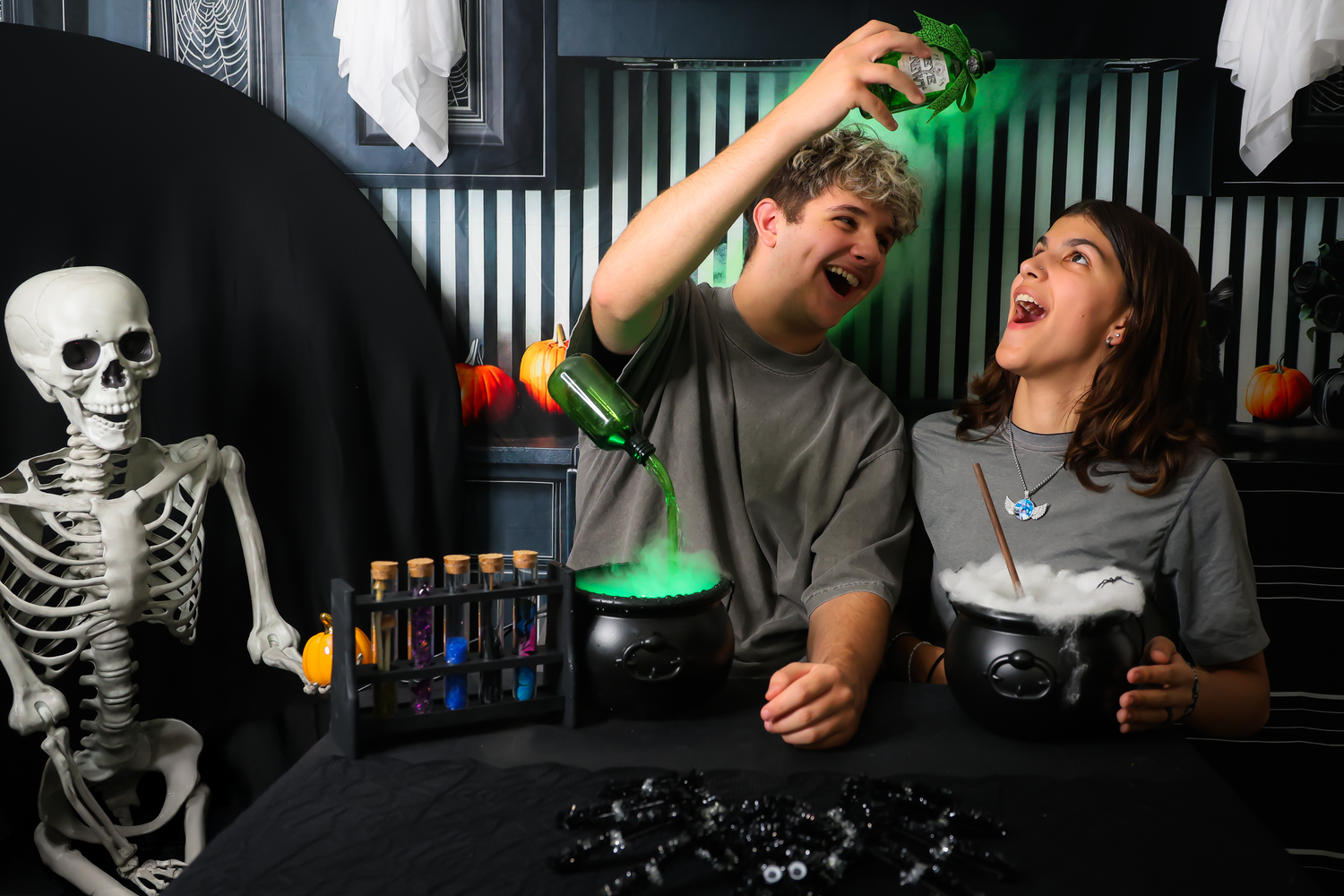 Two teens laugh while doing a spooky Halloween science experiment with colorful potions and a smoking cauldron.