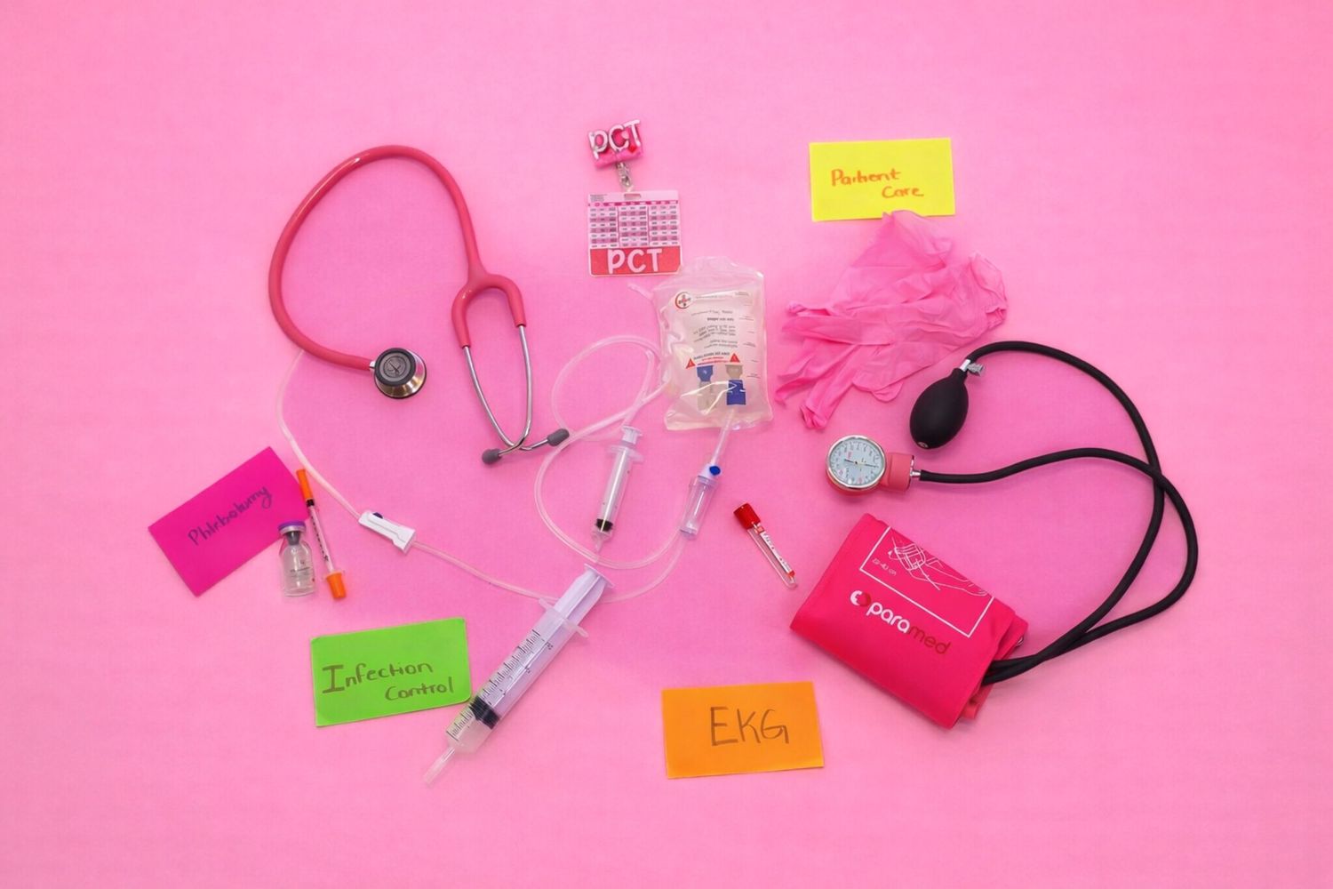 Pink medical supplies including stethoscope, syringes, blood pressure cuff, gloves, and colorful labeled notes on pink background.