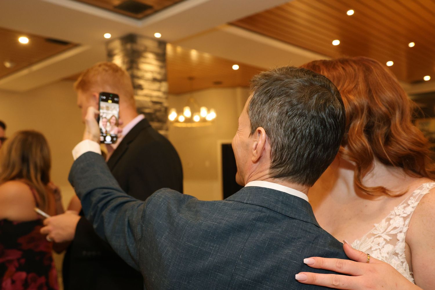 A wedding couple and guests dance together on a wooden floor at an elegant reception venue with warm lighting.