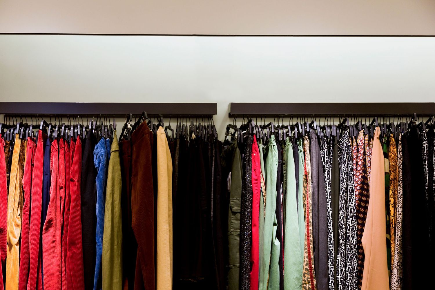 Colorful dresses and garments hanging on black clothing rack against beige wall.