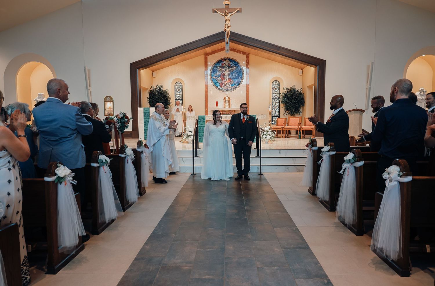 Wedding ceremony in progress at a small chapel with guests seated in pews and a cross visible at the altar.
